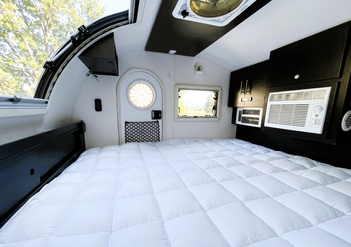 Cozy RV rental sleeping area: a plush white bed, windows, AC, and fan for comfort on your road trip.. nuCamp T@G 2022