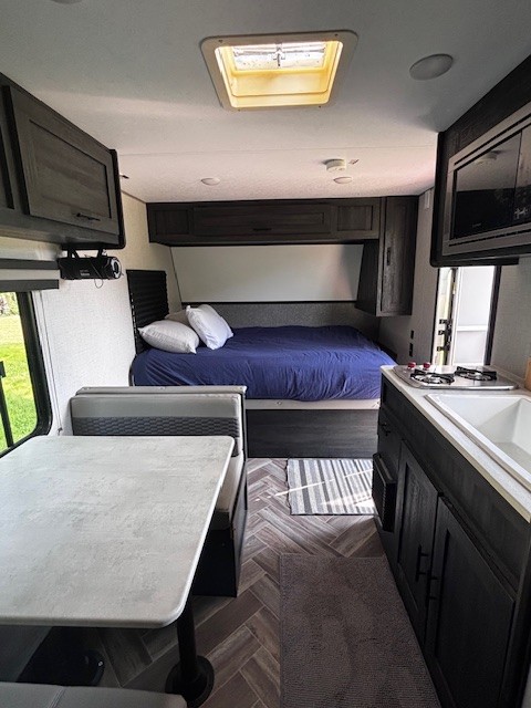 Inside this clean rv rental, a bedroom, dinette with table, and compact kitchen with sink/stove are visible.. Forest River Wildwood 2020