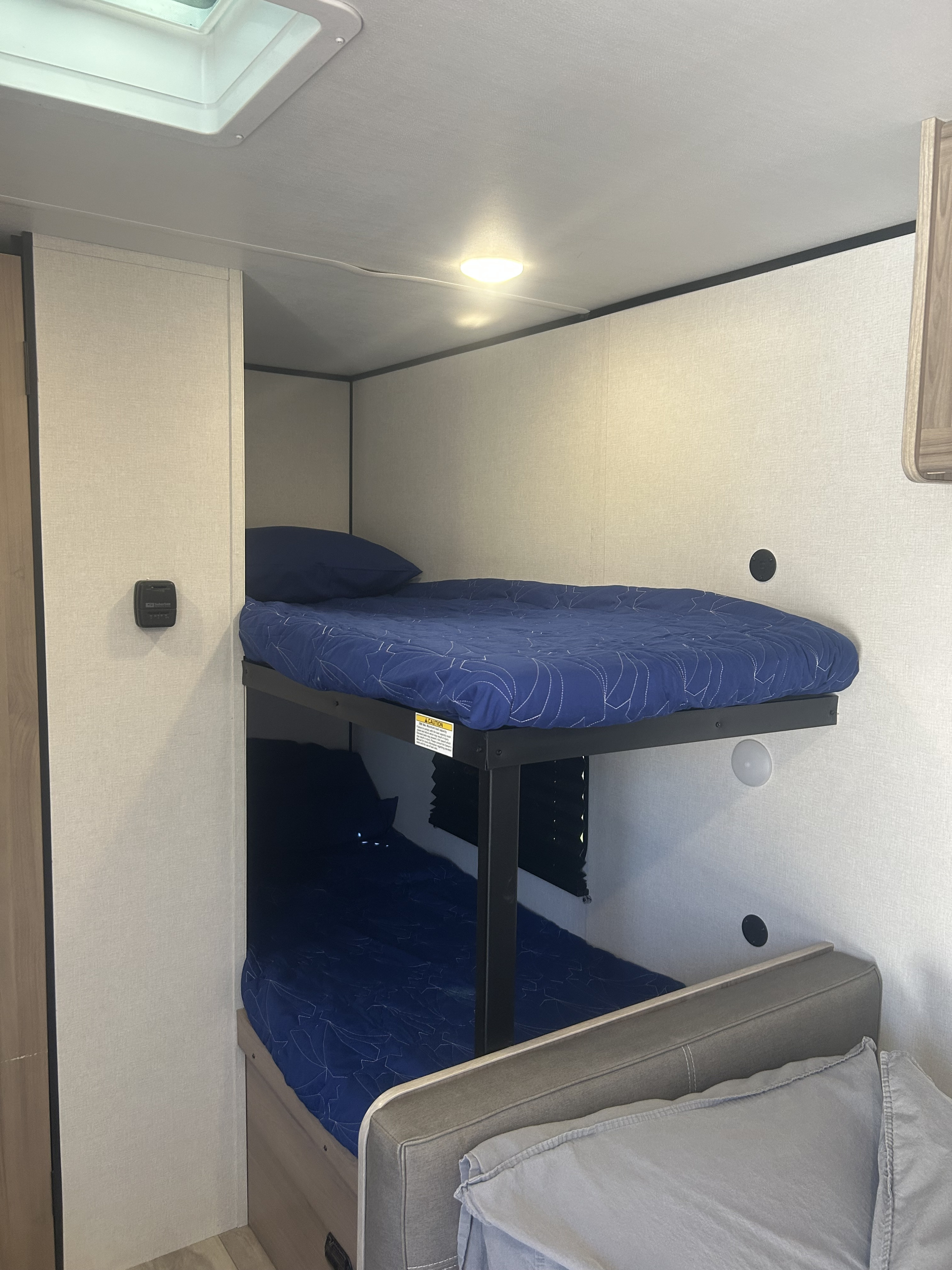Inside an RV rental: Compact bunk beds with blue bedding, a skylight, and thermostat for a comfortable sleeping area.. Keystone Coleman 17b 2025