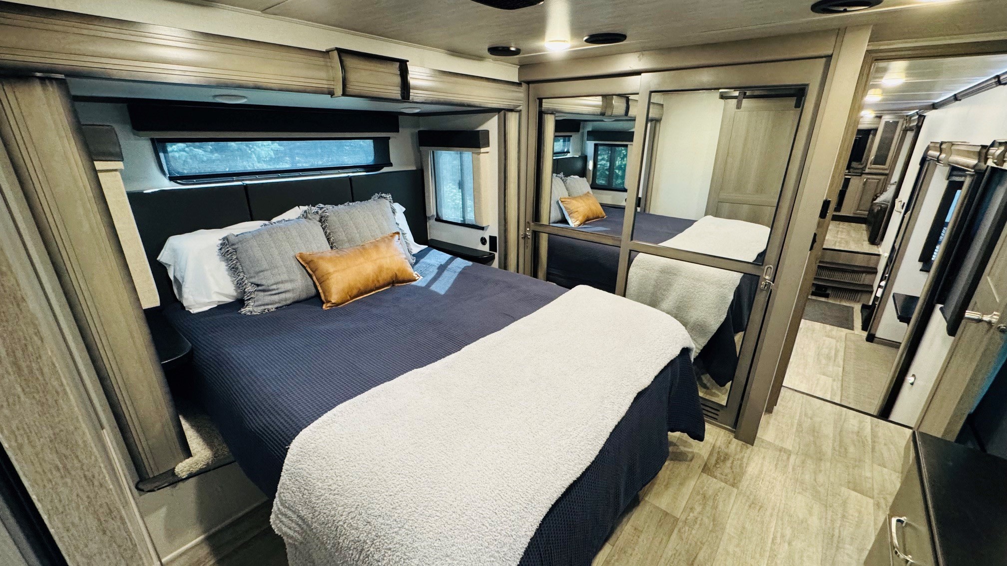 Spacious RV rental bedroom featuring a large bed with pillows, windows, and a mirrored wardrobe, ideal for comfortable travel.. Keystone RV Montana 2021