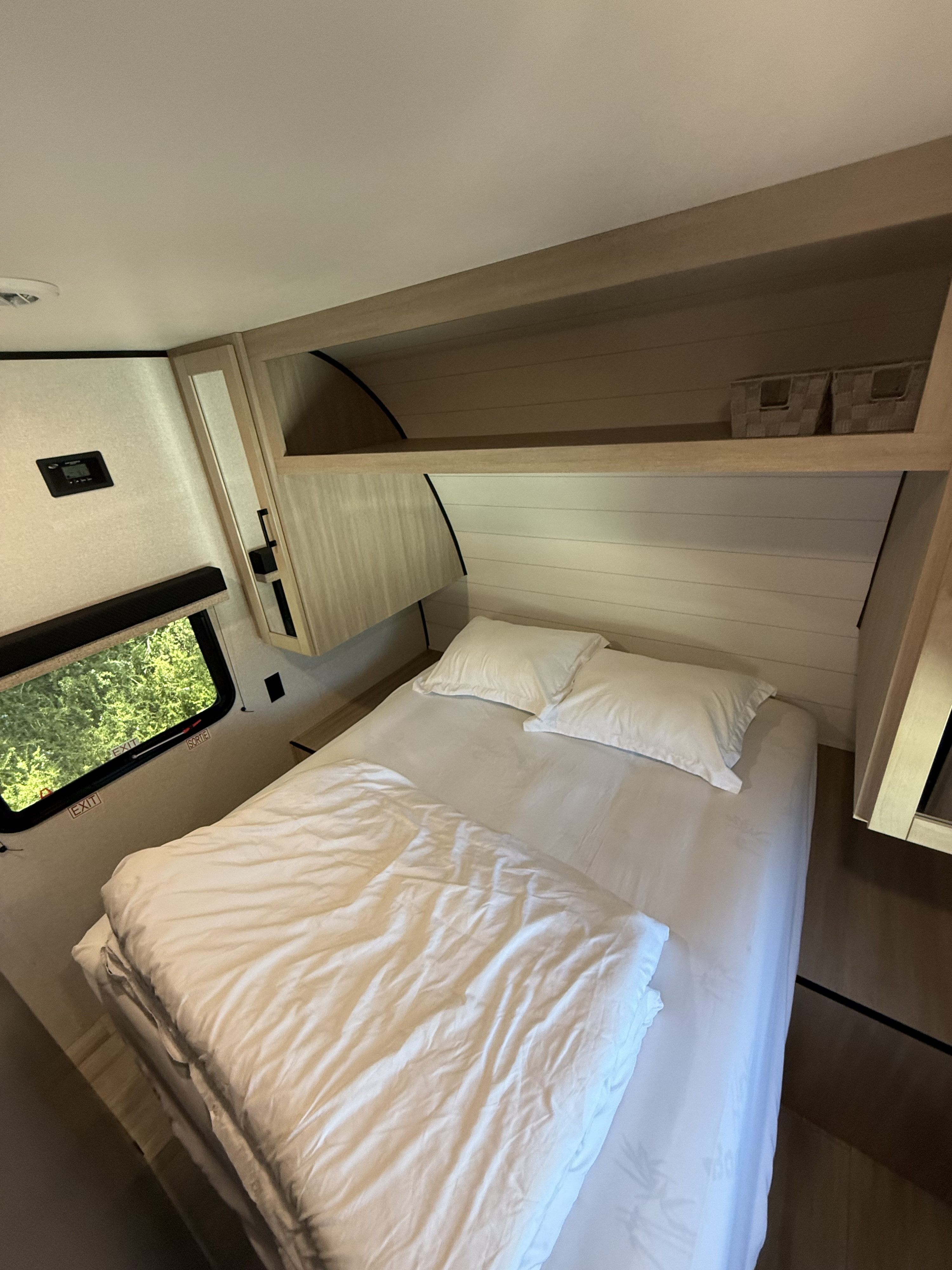 Explore this RV rental bedroom's cozy interior, featuring a comfortable bed, window with nature view, and overhead storage.. Heartland Powler 2026