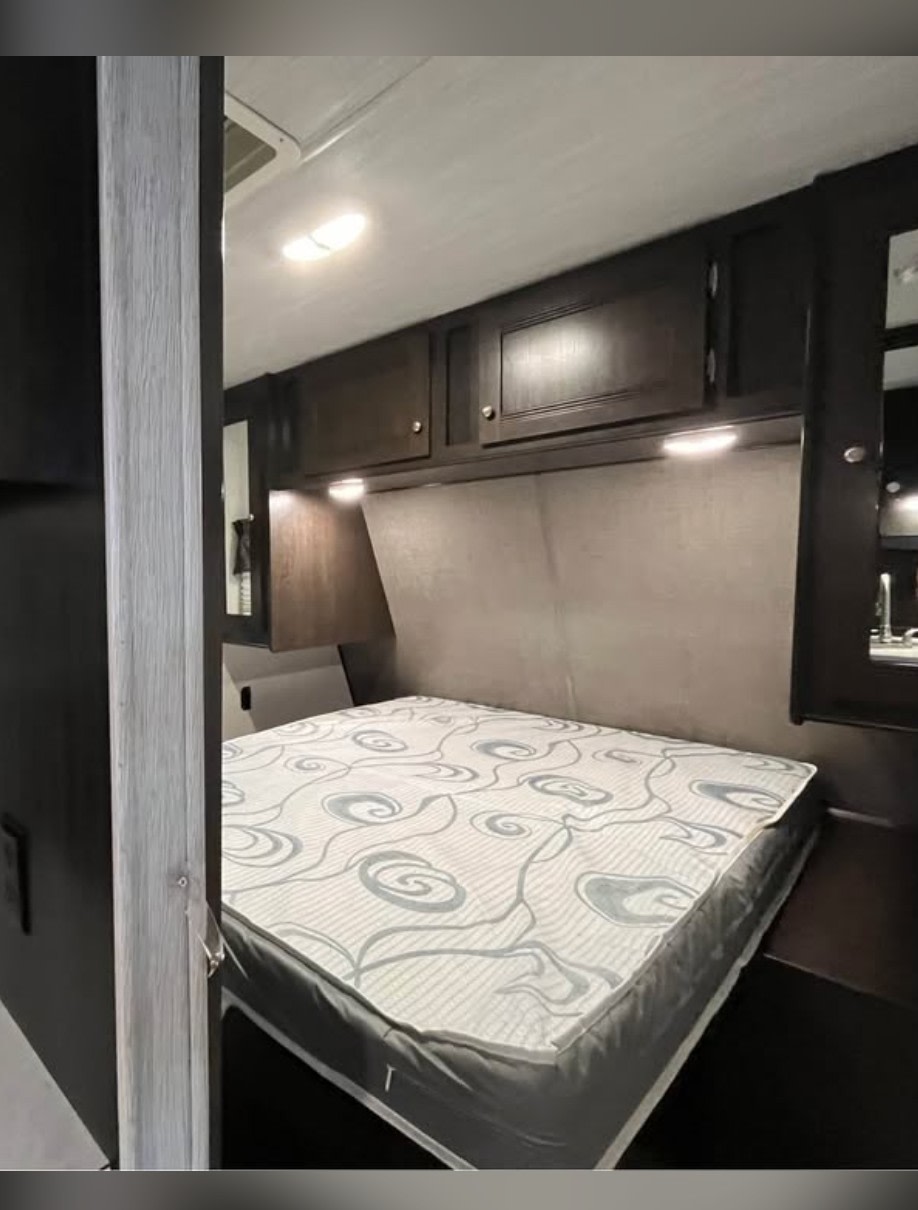 Interior of an RV rental bedroom featuring a mattress, dark cabinets, and reading lights. Ideal compact sleeping space.. Heartland RVs Prowler 2019