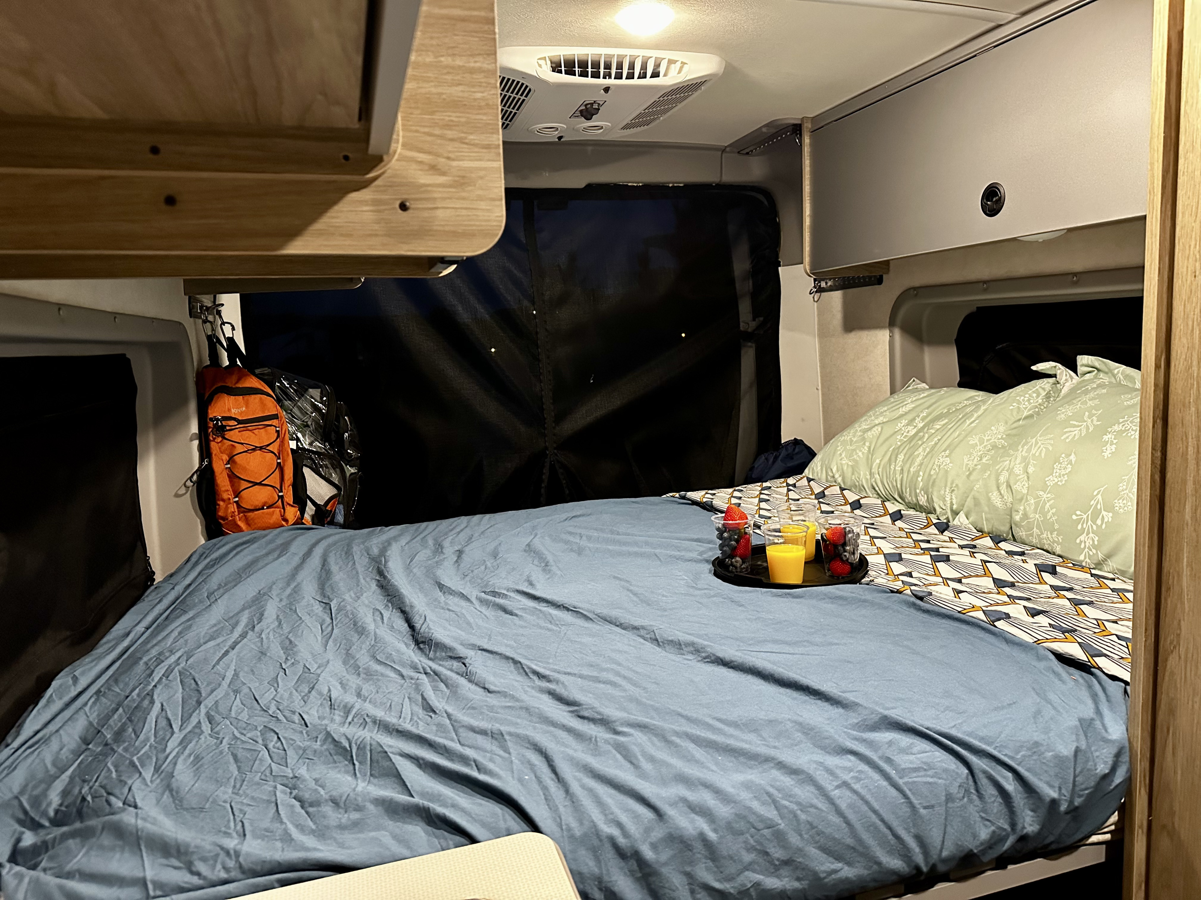 Cozy RV rental camper van bedroom. Breakfast in bed with juice and berries. Pillows and storage complete the cozy camping setup.. Winnebago Solis 59PX 2023