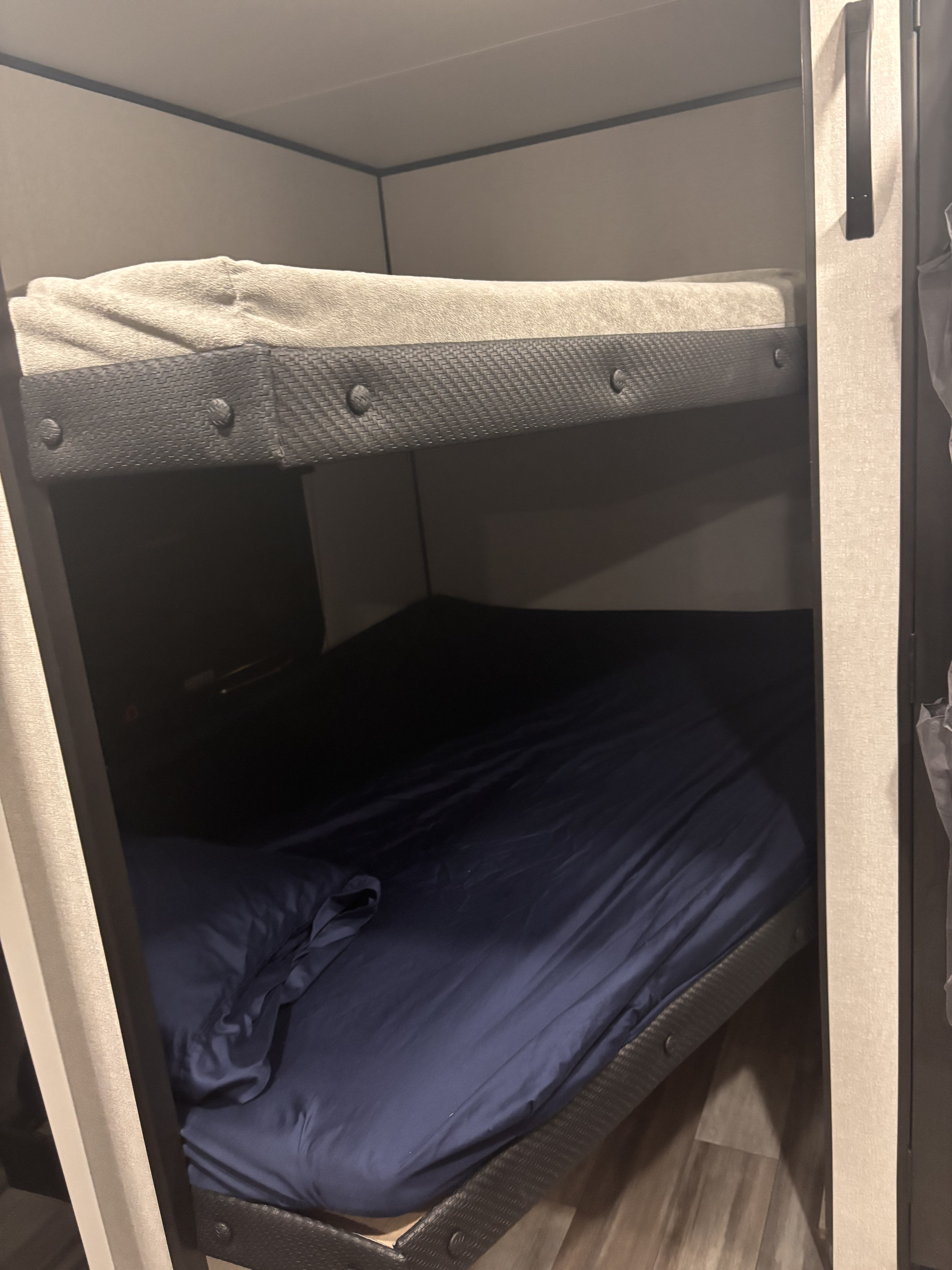 Cozy bunk beds in an RV rental, featuring a grey top mattress and dark blue sheets on the bottom bunk, perfect for travel.. Jayco Jay Flight SLX Sport Edition 2026