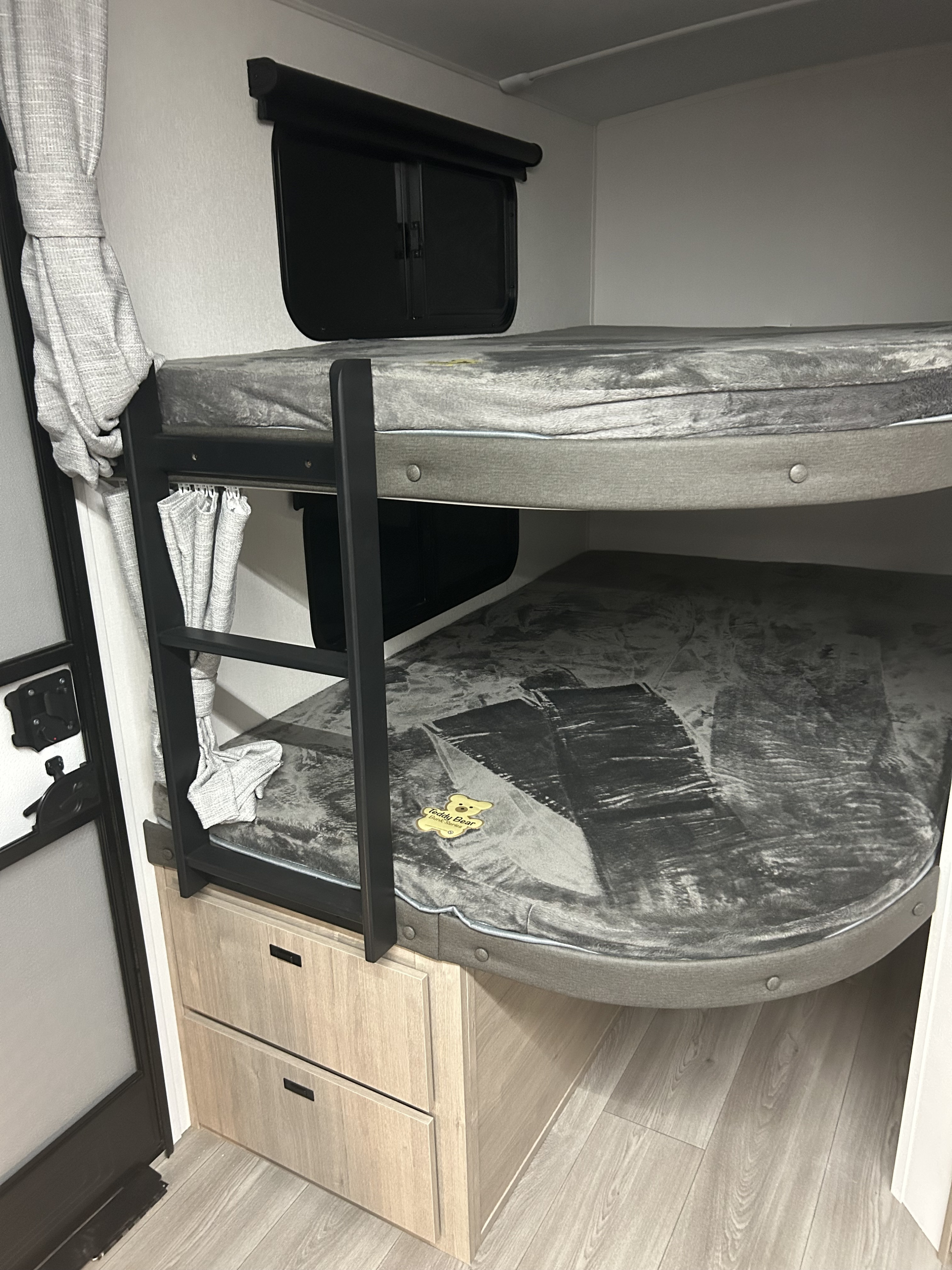 RV rental bunk beds: grey mattresses, black ladder, and wood storage drawers, ideal for comfortable family camping.. Grand Design Imagine 2026