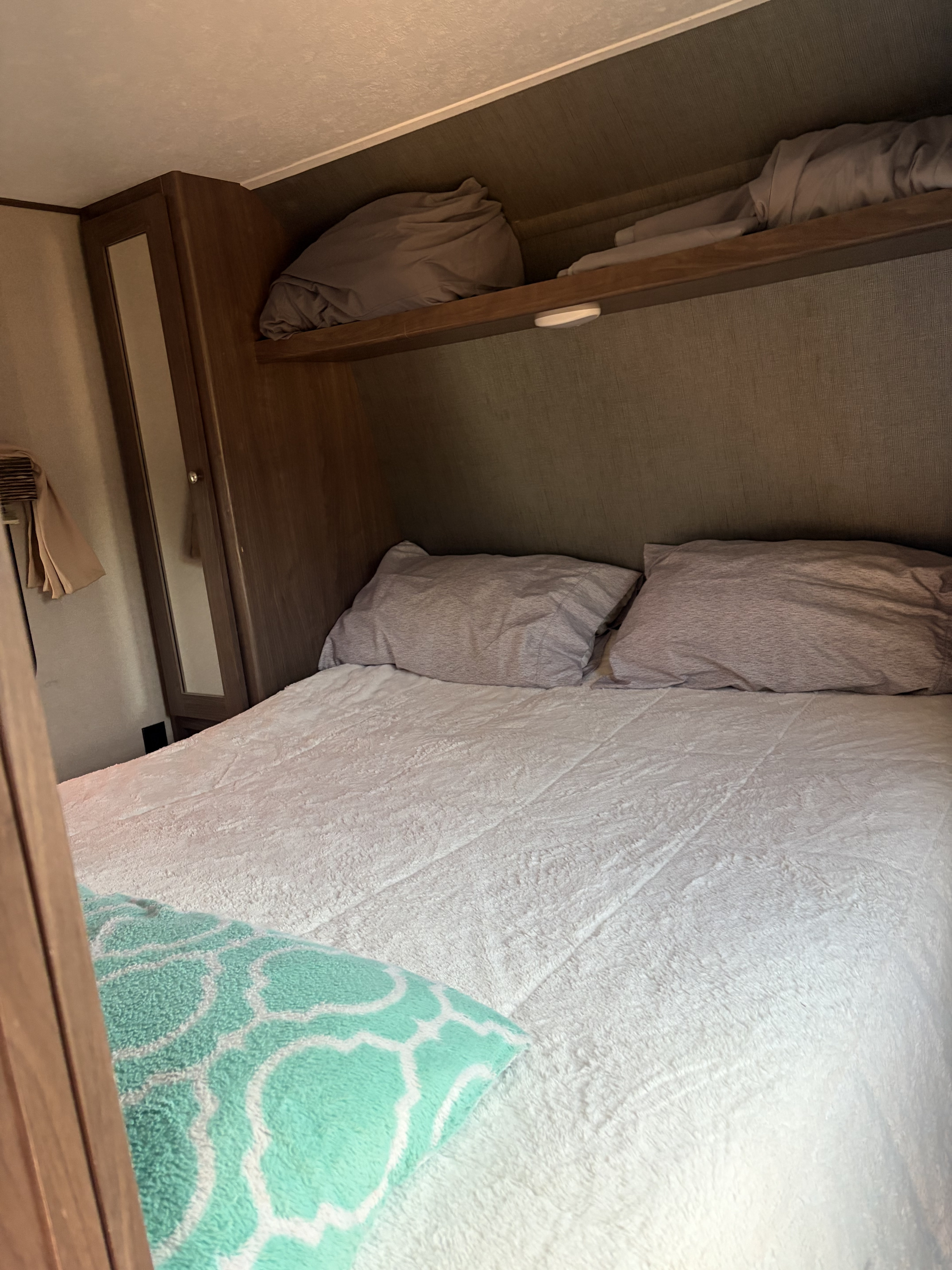 Cozy RV rental bedroom featuring a bed with grey pillows, a white blanket, and a teal patterned throw, plus overhead storage.. Keystone RV Hideout LHS 2018