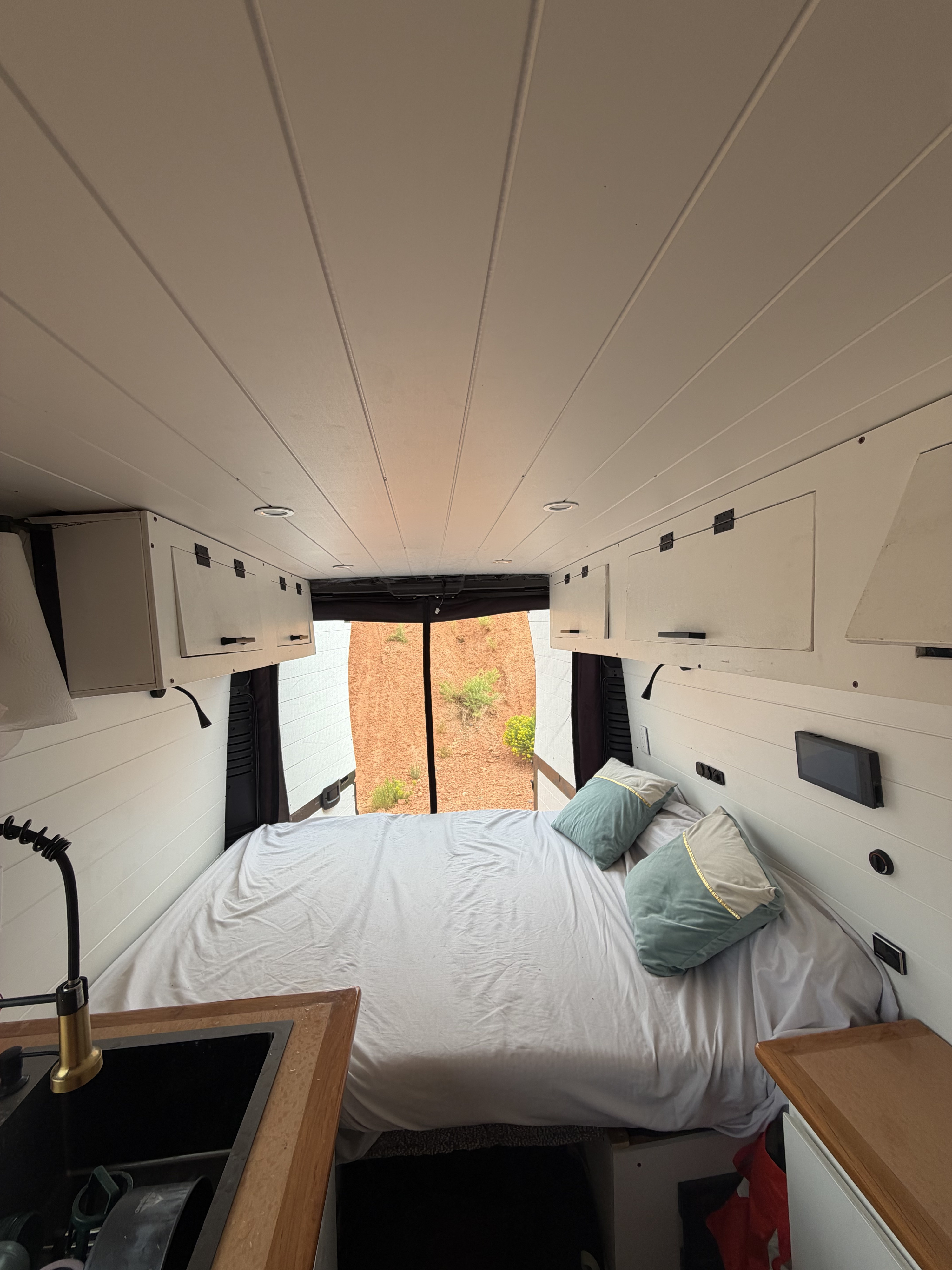 RV rental interior: A cozy bed in the back, a kitchen sink on the left, with open rear doors showing a desert view.. Dodge Ram 1500 2017