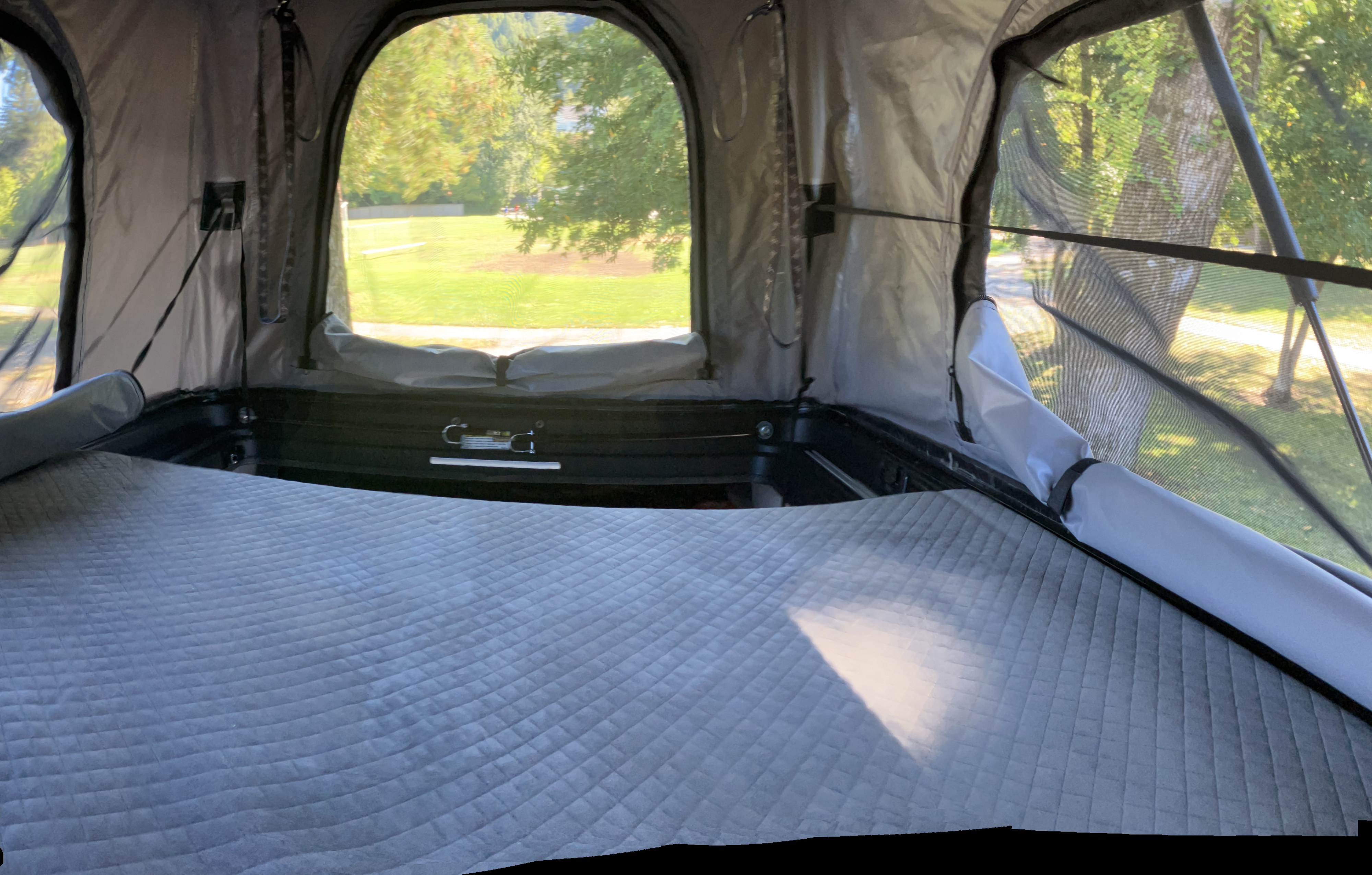 Cozy interior of an RV rental tent with a quilted mattress, offering a scenic outdoor view through mesh windows. Ideal for camping.. Winnebago Solis 2025