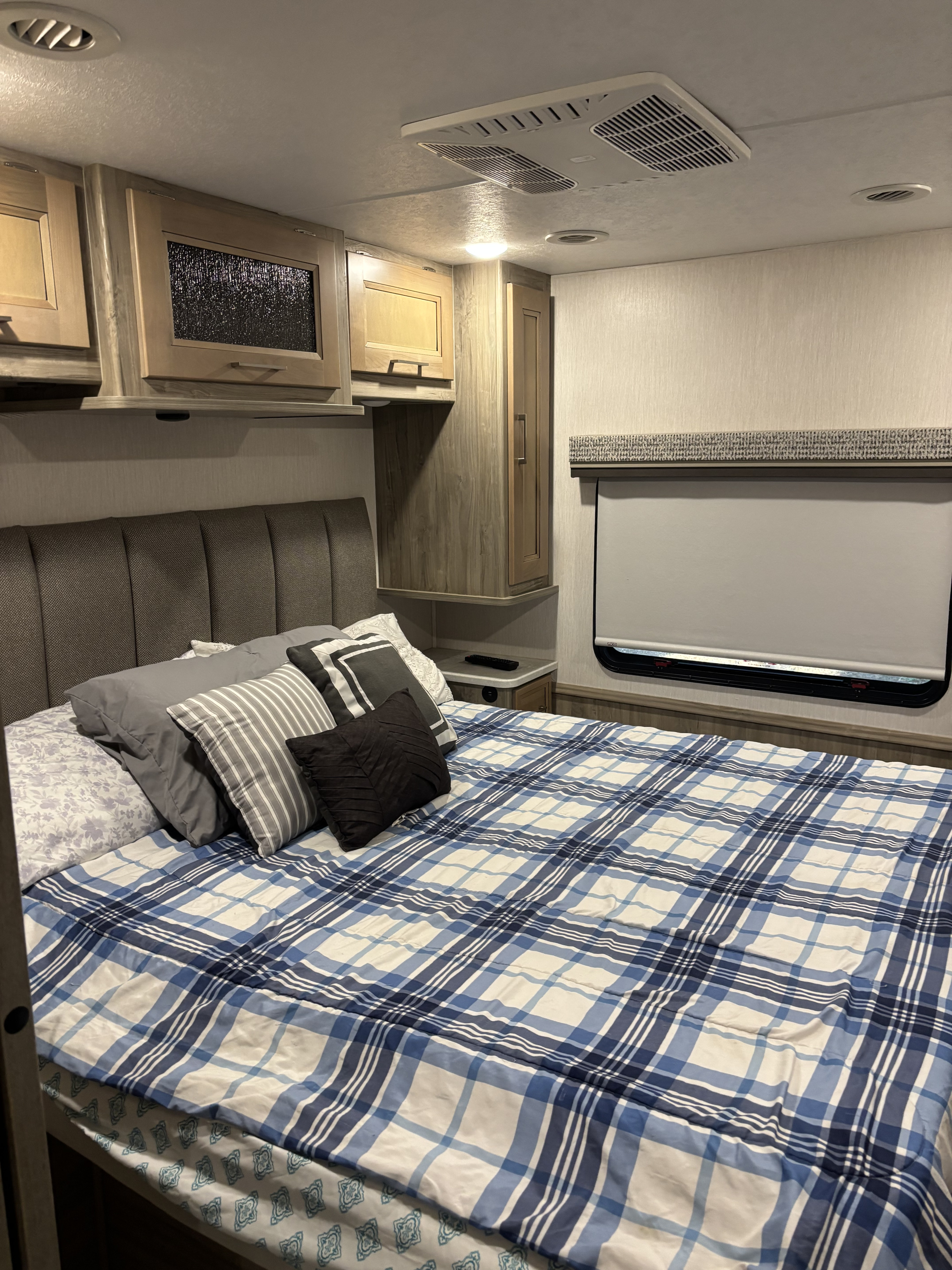 Inside a comfy RV rental bedroom: plush bed, plaid comforter, storage cabinets, and window with shade.. Coachmen Mirada 32ss 2020