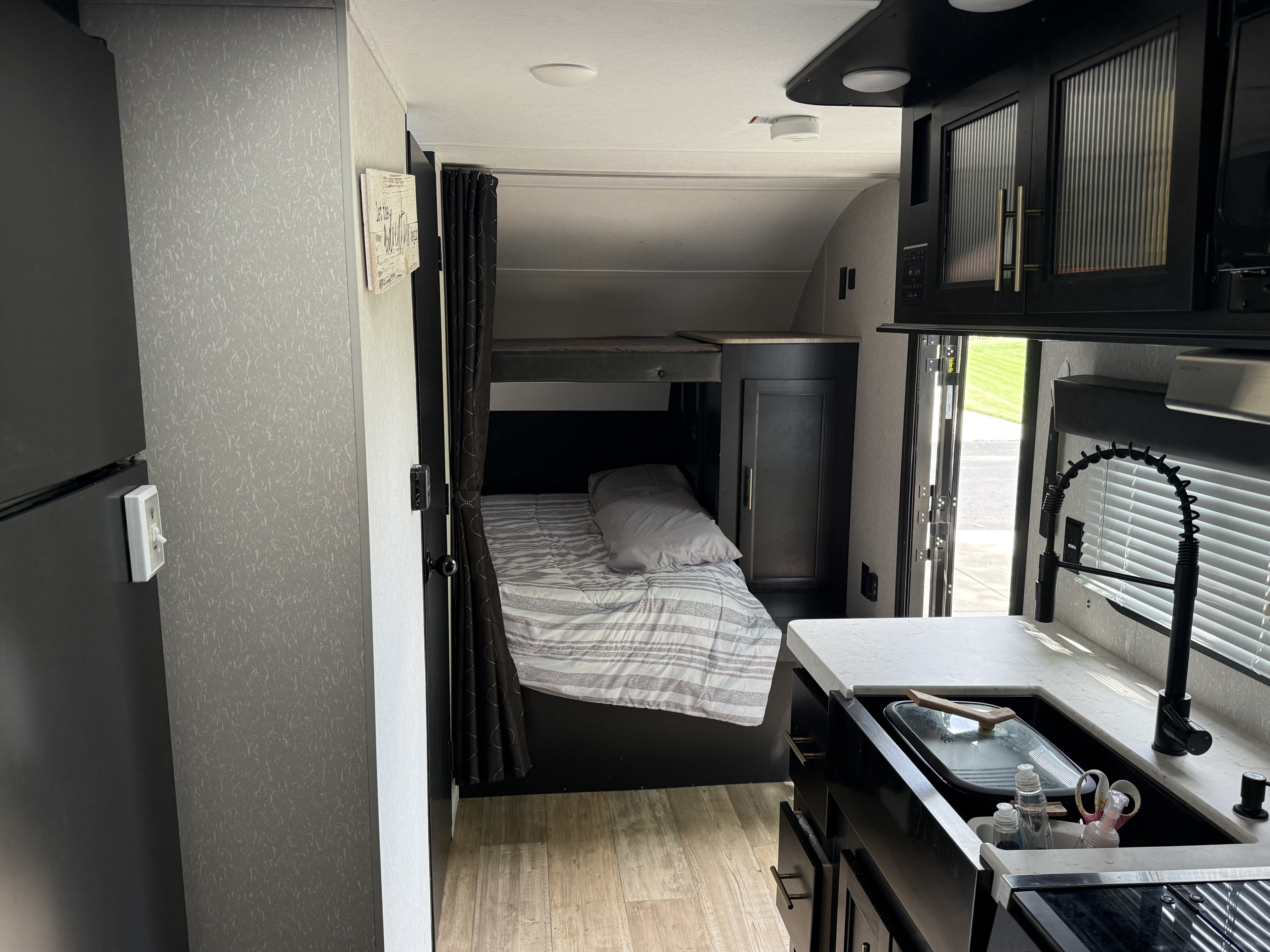 Inside a modern rv rental with dark cabinetry: kitchen sink, pull-down faucet, and bunk beds.. Forest River Cherokee Grey Wolf 2021