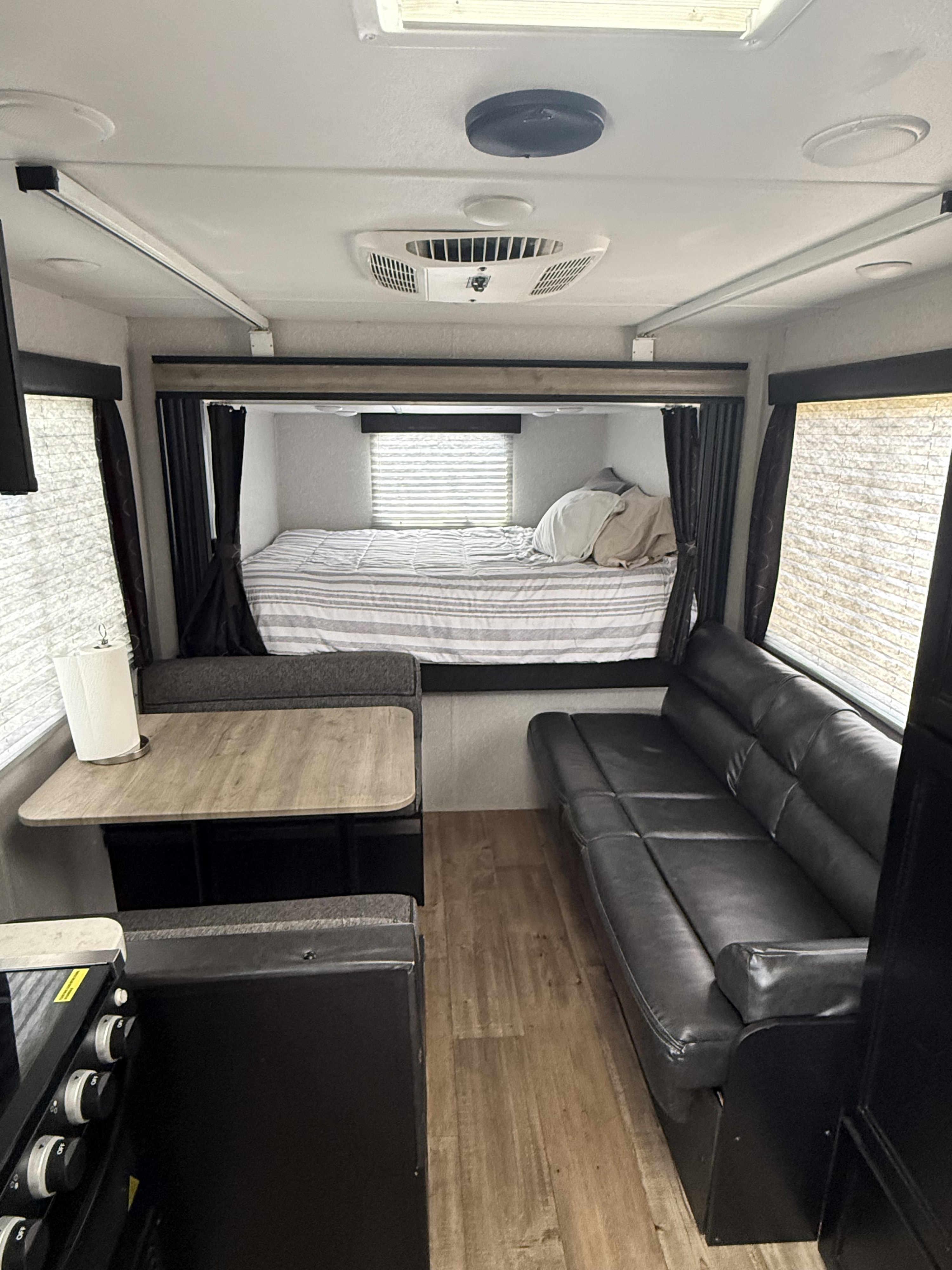 RV rental interior featuring a bed at the back, a dinette on the left, and a black faux leather sofa on the right.. Forest River Cherokee Grey Wolf 2021