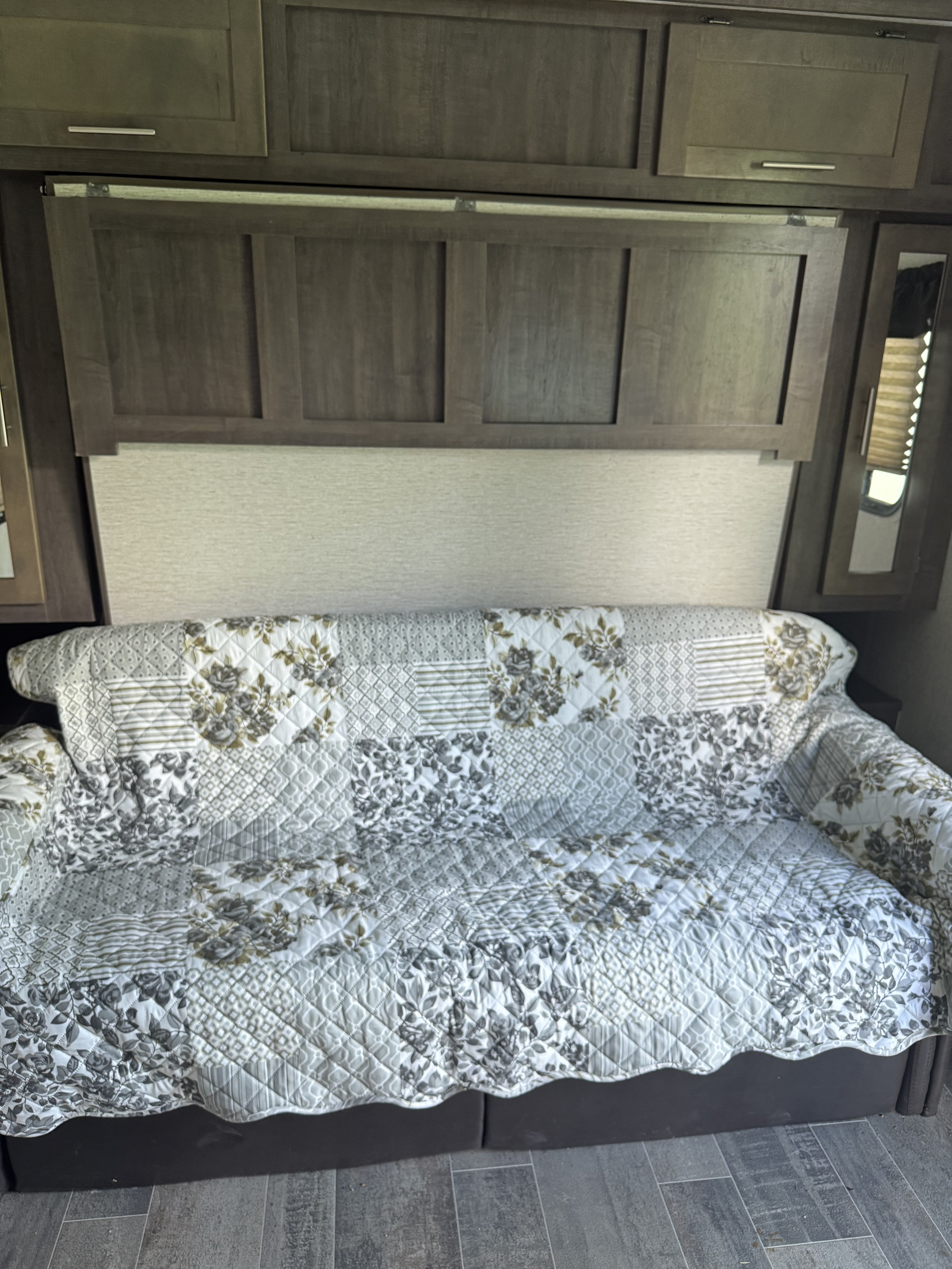 This RV rental interior features a sofa covered with a grey and white floral quilted throw, set against wooden cabinets.. Crossroads RV Sunset Trail Super Lite 2019