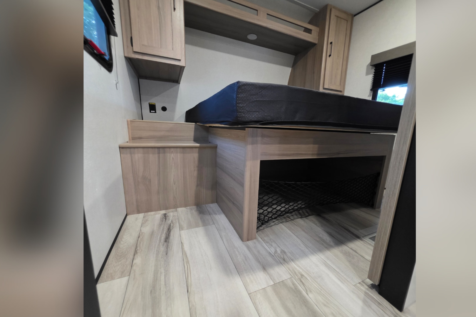 Cozy bunk bed area in an RV rental, featuring built-in steps, an under-bed storage net, and light wood cabinetry.. Keystone Coleman 22BX 2027