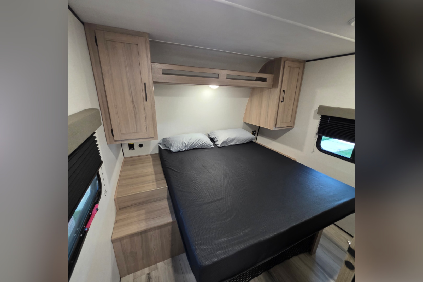 RV rental bedroom interior: a comfy bed with black mattress, overhead cabinets, window, and practical steps.. Keystone Coleman 22BX 2027
