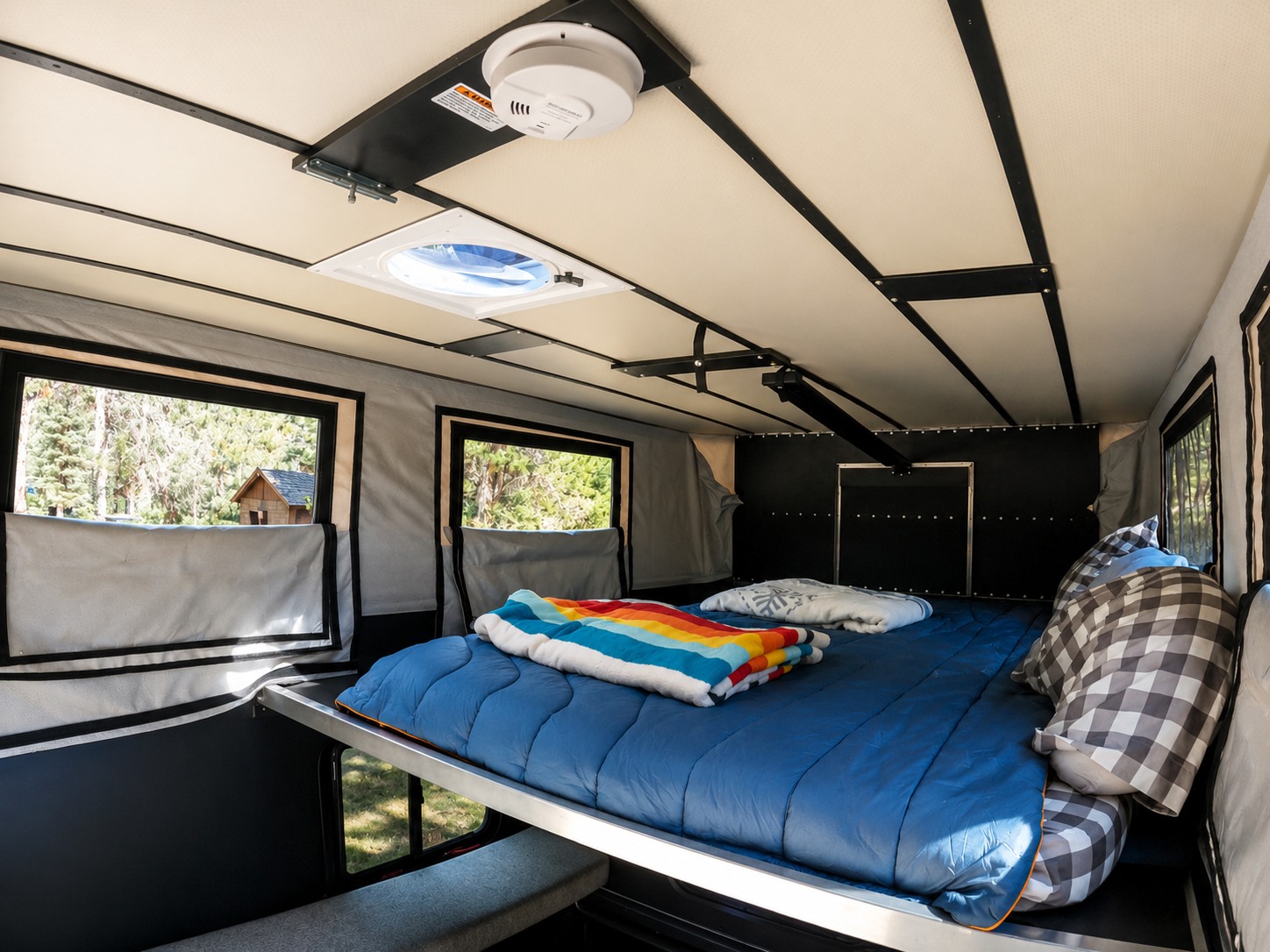 Bright rv rental interior showing a comfortable bed with a colorful blanket, windows with forest views, and a ceiling vent.. Four Wheel Campers Shell Models 2020