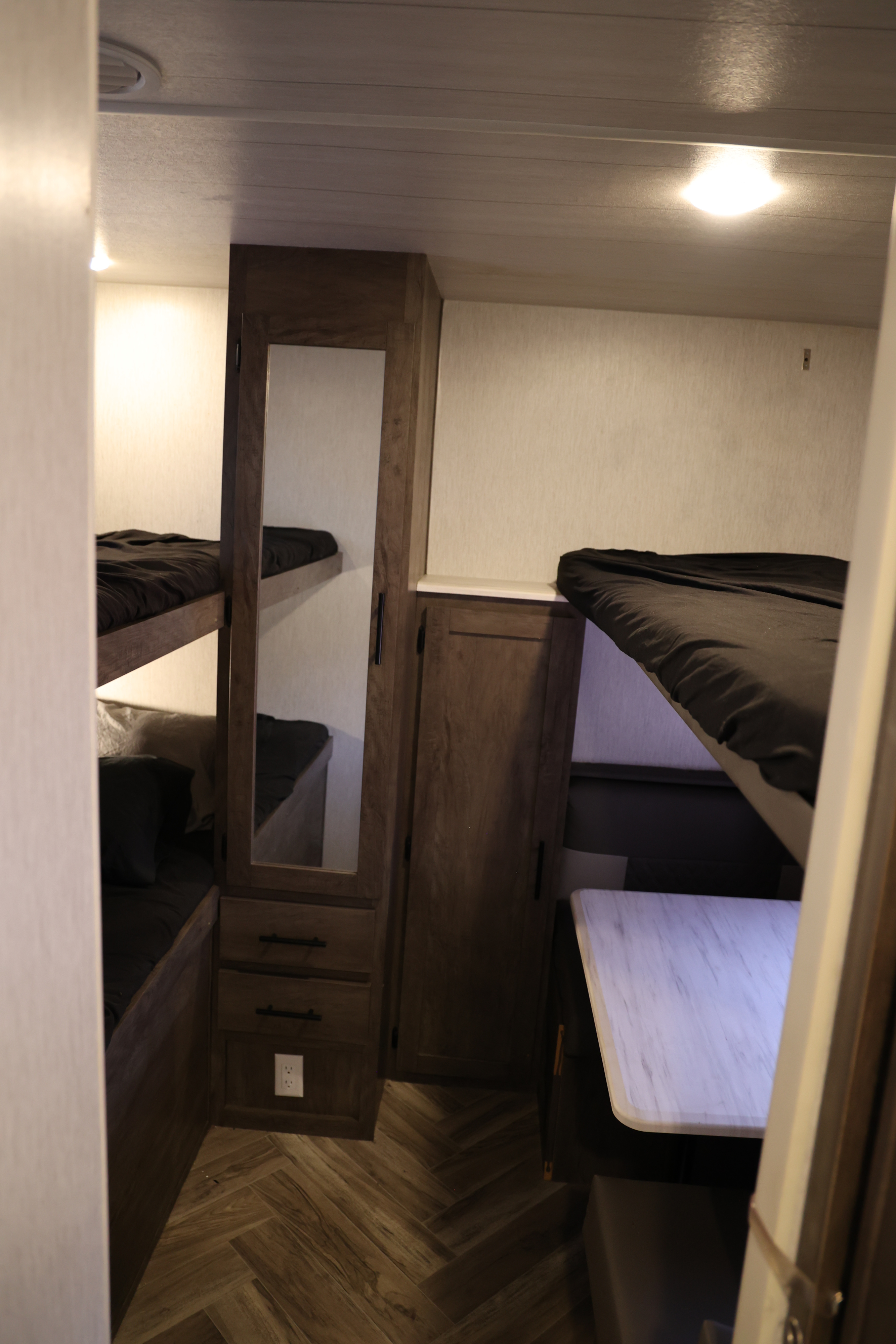 This RV rental interior shows dark bunk beds, a mirrored cabinet, and a white dinette table on herringbone flooring.. Forest River Salem Cruise Lite 2022