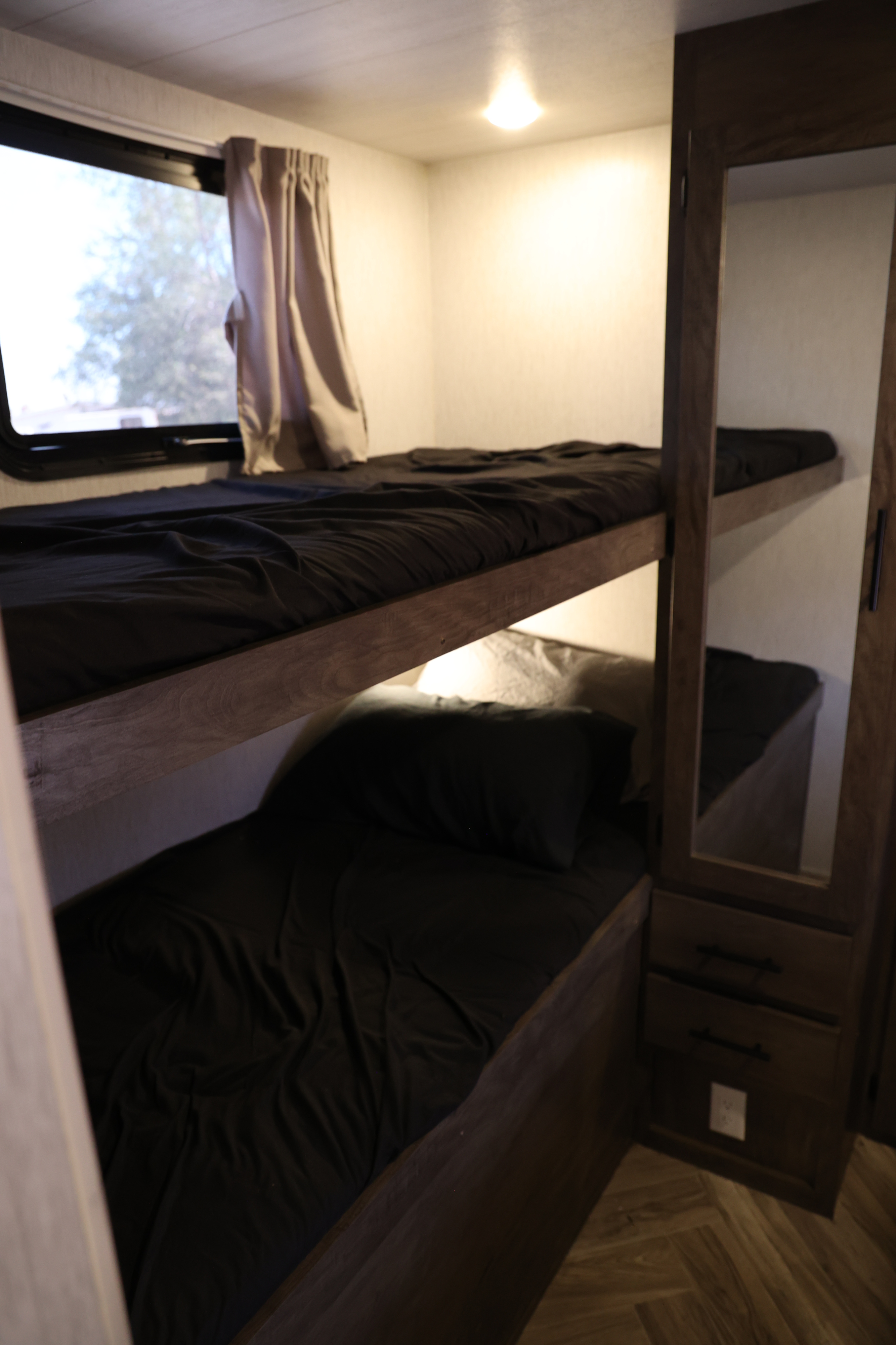 Cozy bunk beds with dark bedding and a window, perfect for an RV rental. Features built-in storage and ambient lighting.. Forest River Salem Cruise Lite 2022