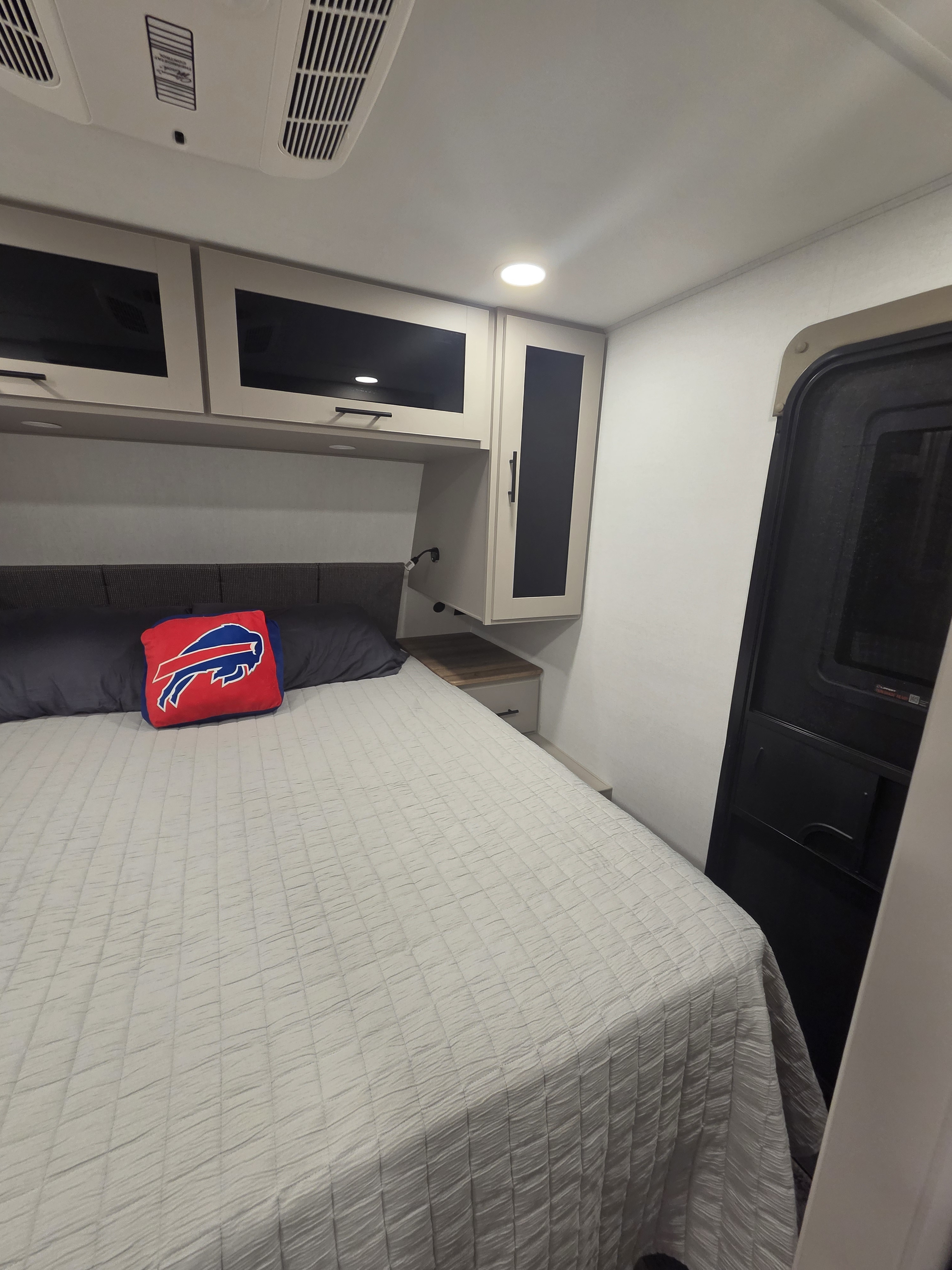 This cozy RV rental bedroom features a comfortable bed, overhead storage, bedside table, and ceiling air conditioning.. Alliance RV Delta 2026