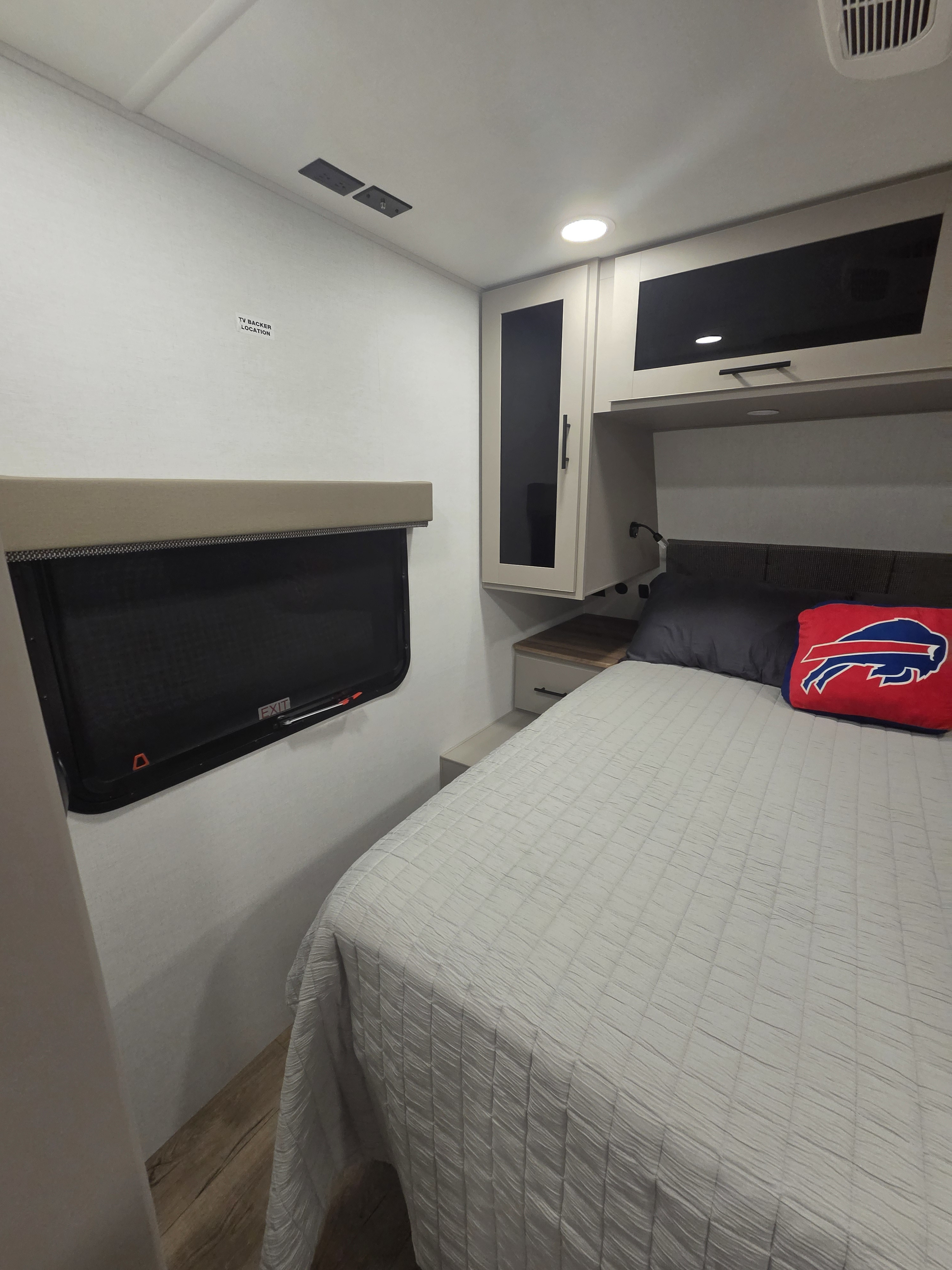 Comfortable RV rental bedroom with a bed, cabinets, and a window. A Buffalo Bills pillow adds a personal touch.. Alliance RV Delta 2026