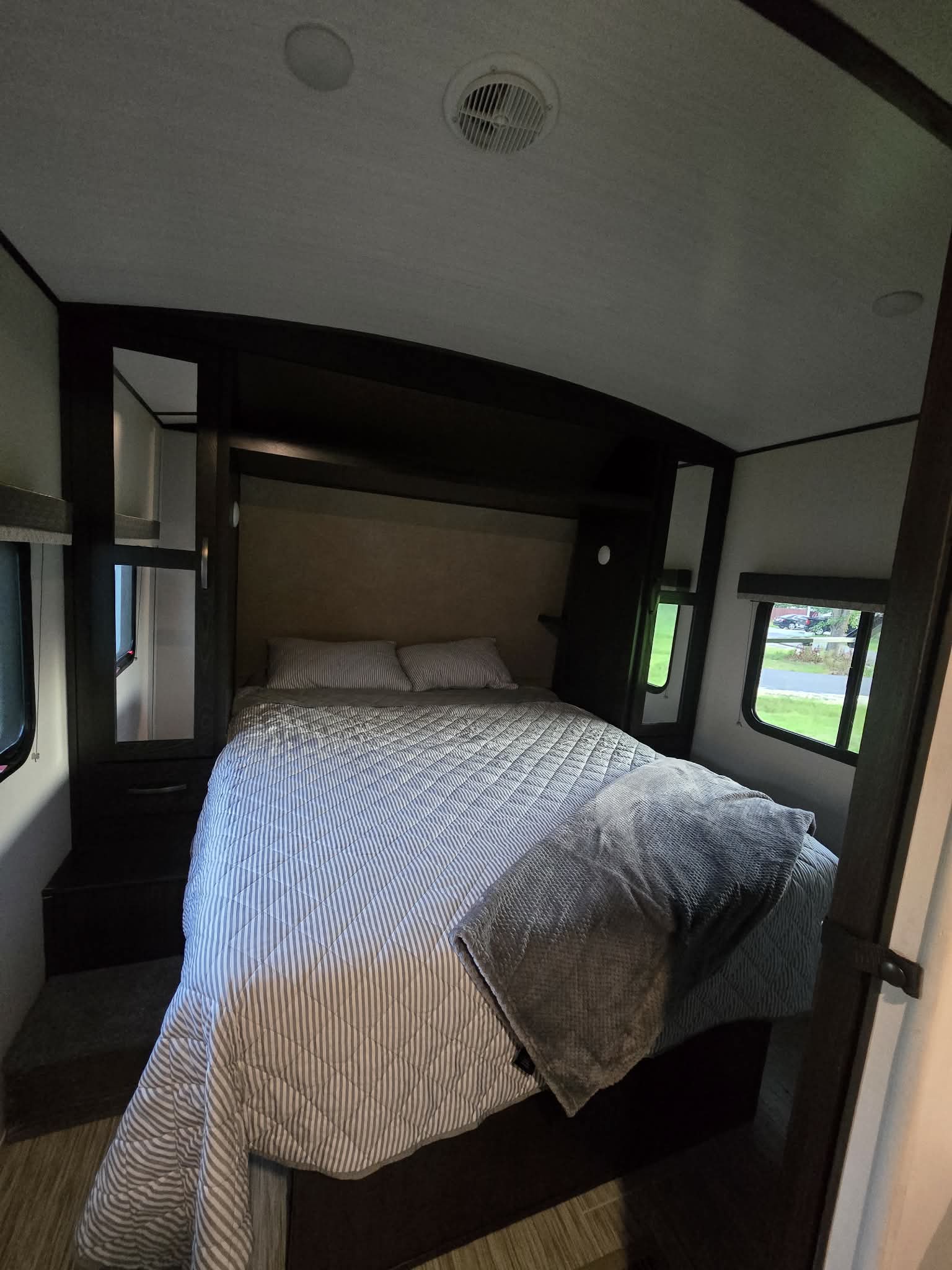 Cozy RV rental bedroom with striped bedding, built-in storage, windows, and ceiling lights/vent, perfect for travel.. Forest River Surveyor Legend 2020