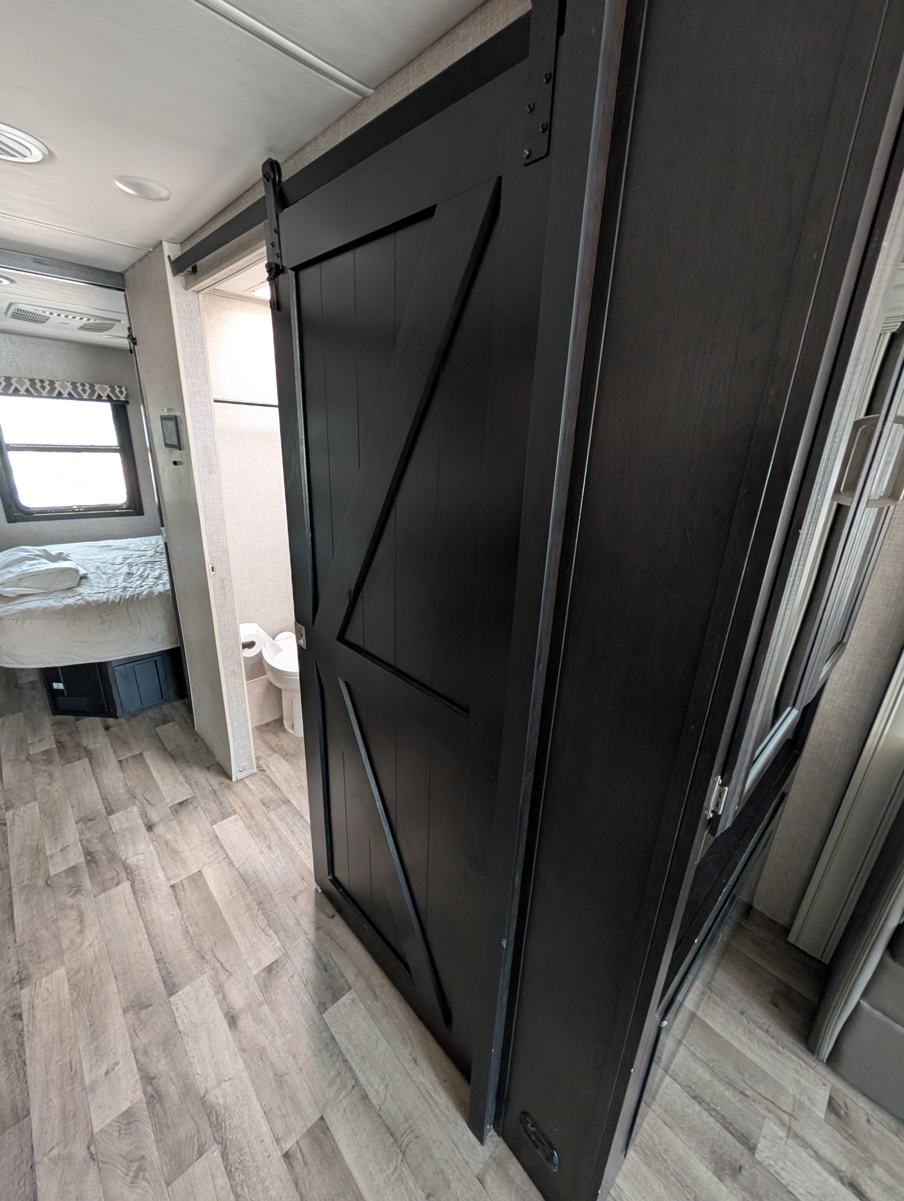 RV rental interior: modern black barn door, separating bedroom & bathroom, on light wood-look floor.. Entegra Coach Vision XL 2022