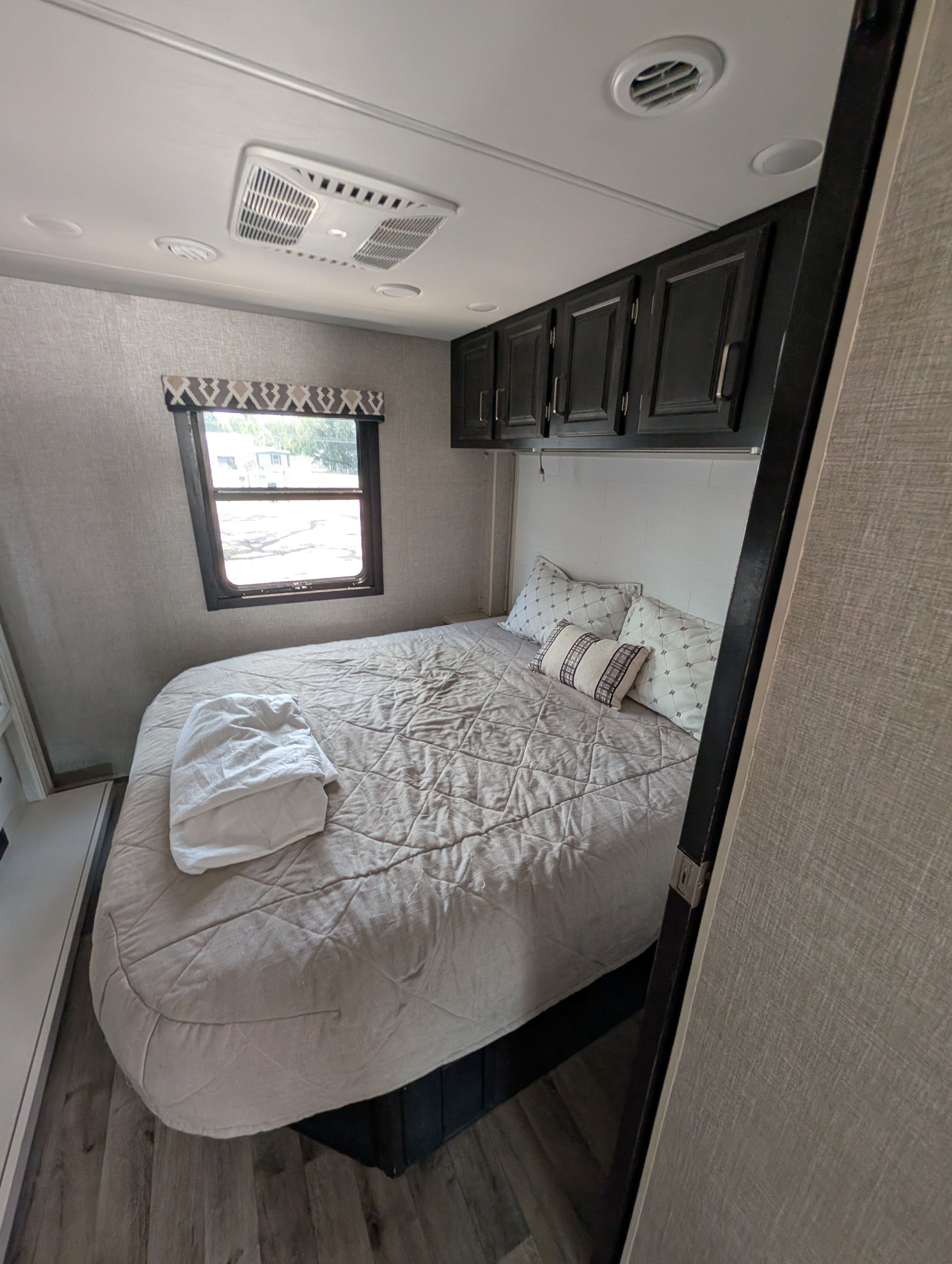 Comfortable RV rental bedroom featuring a bed, overhead cabinets, window, and AC, ideal for restful nights on your journey.. Entegra Coach Vision XL 2022