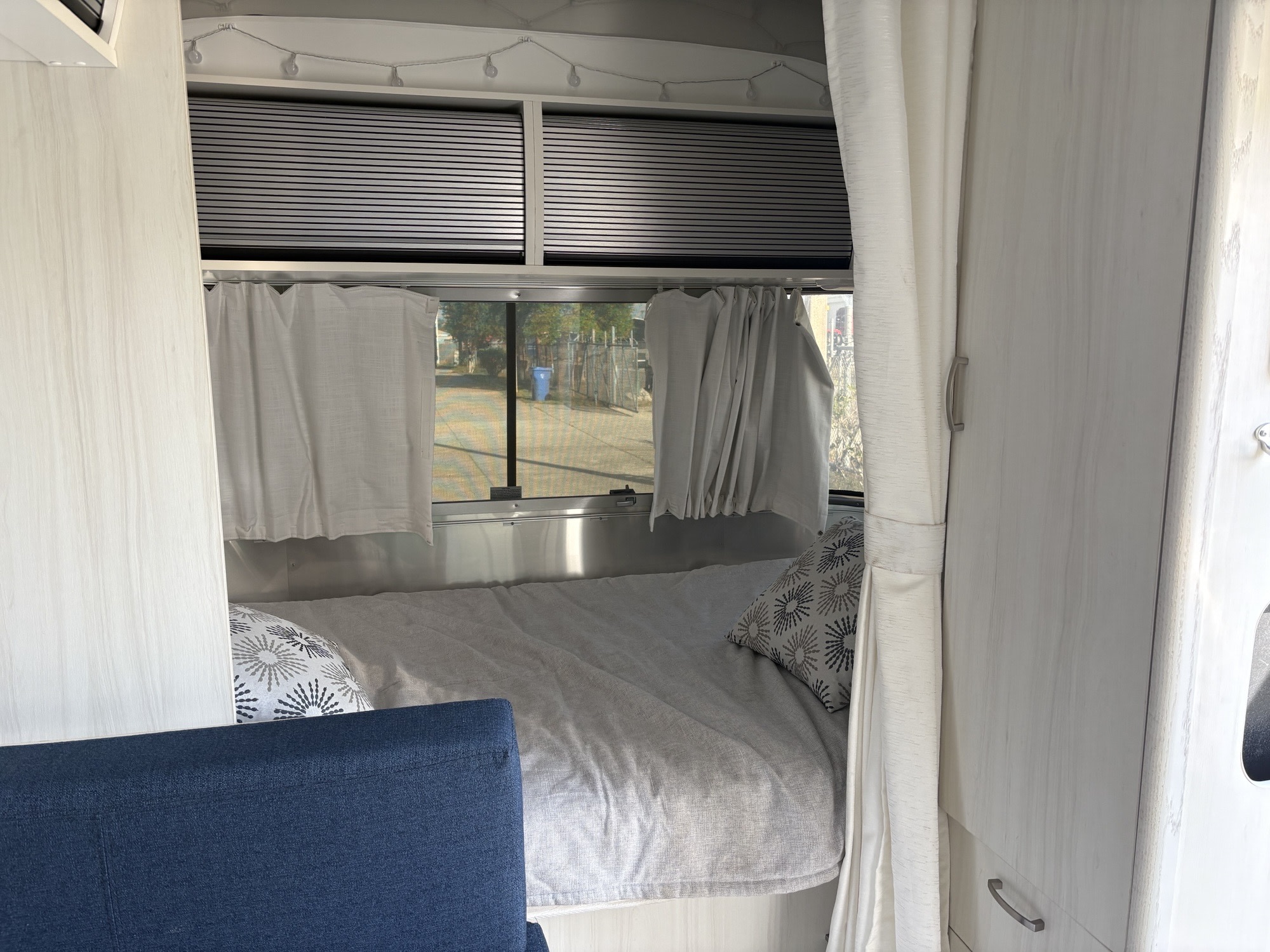 Inside a modern rv rental: a neatly made bed with patterned pillows, window views, and organized overhead storage.. Airstream Bambi 2022