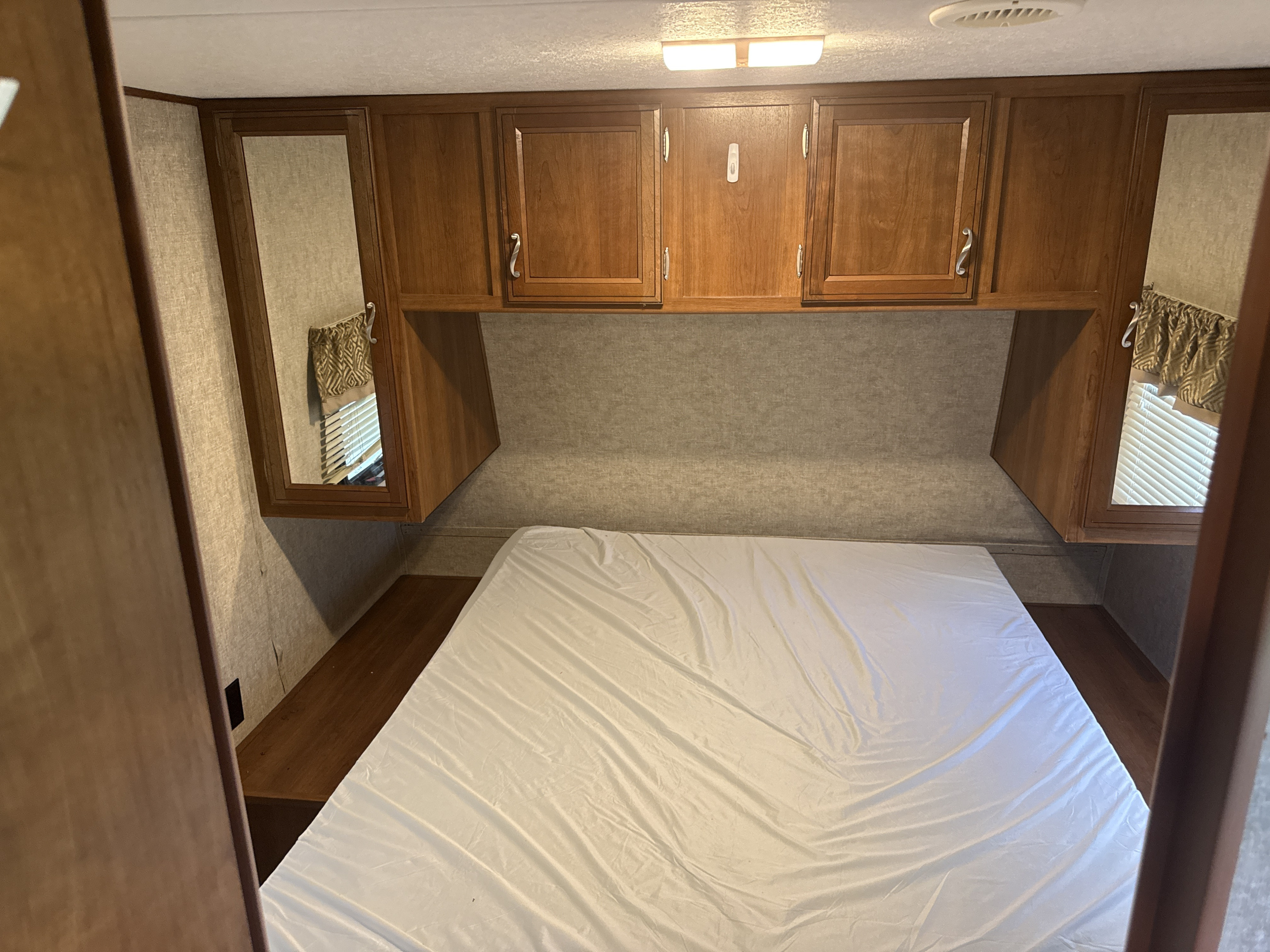 This RV rental bedroom features a comfortable bed, wooden overhead cabinets, and mirrored wardrobes, typical of a camper's sleeping area.. Avenger ATI 2016