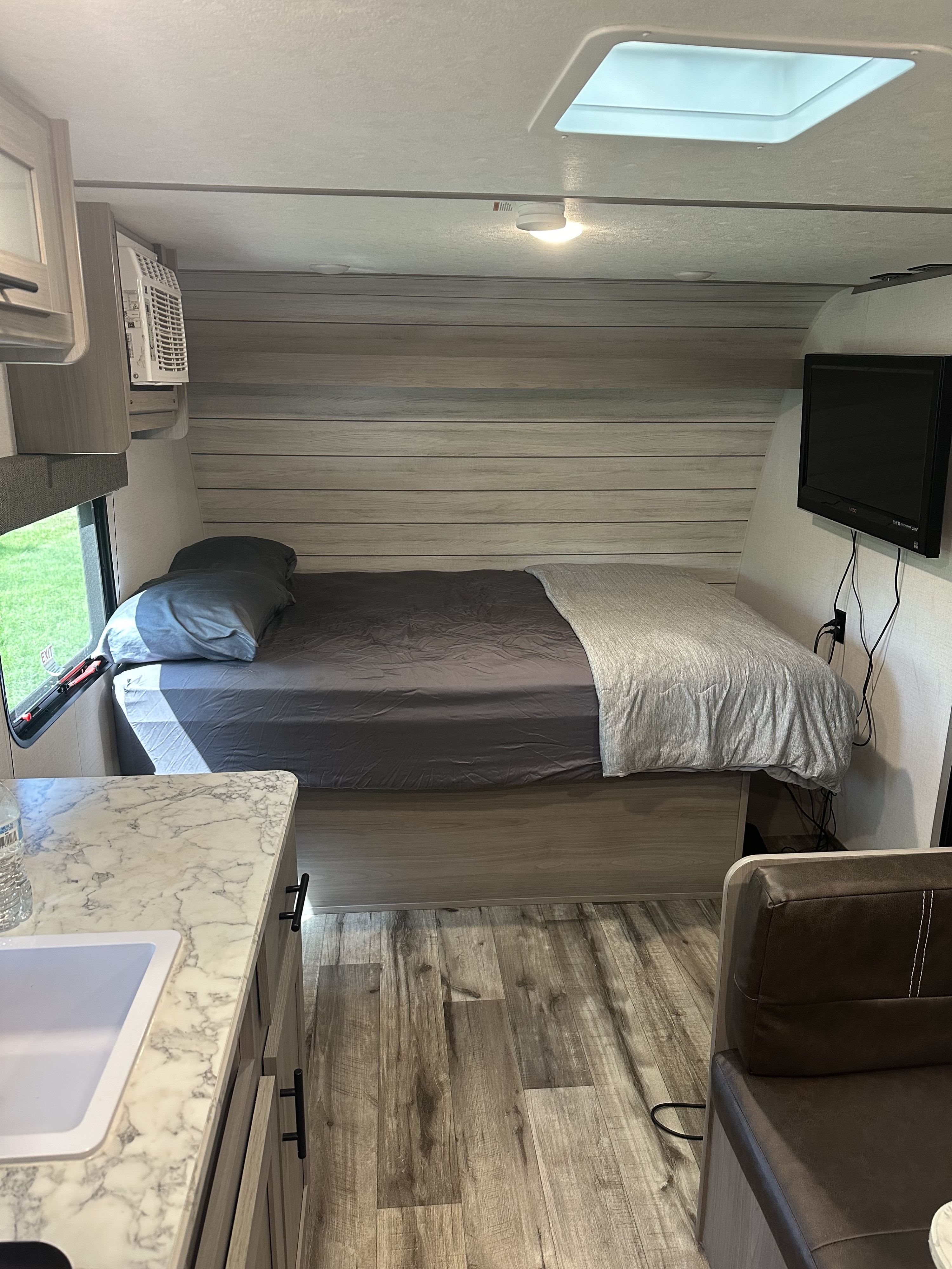 Modern rv rental interior showing a cozy bedroom with bed, AC, TV, and a compact kitchen counter with sink.. Keystone RV Aspen trail 2024