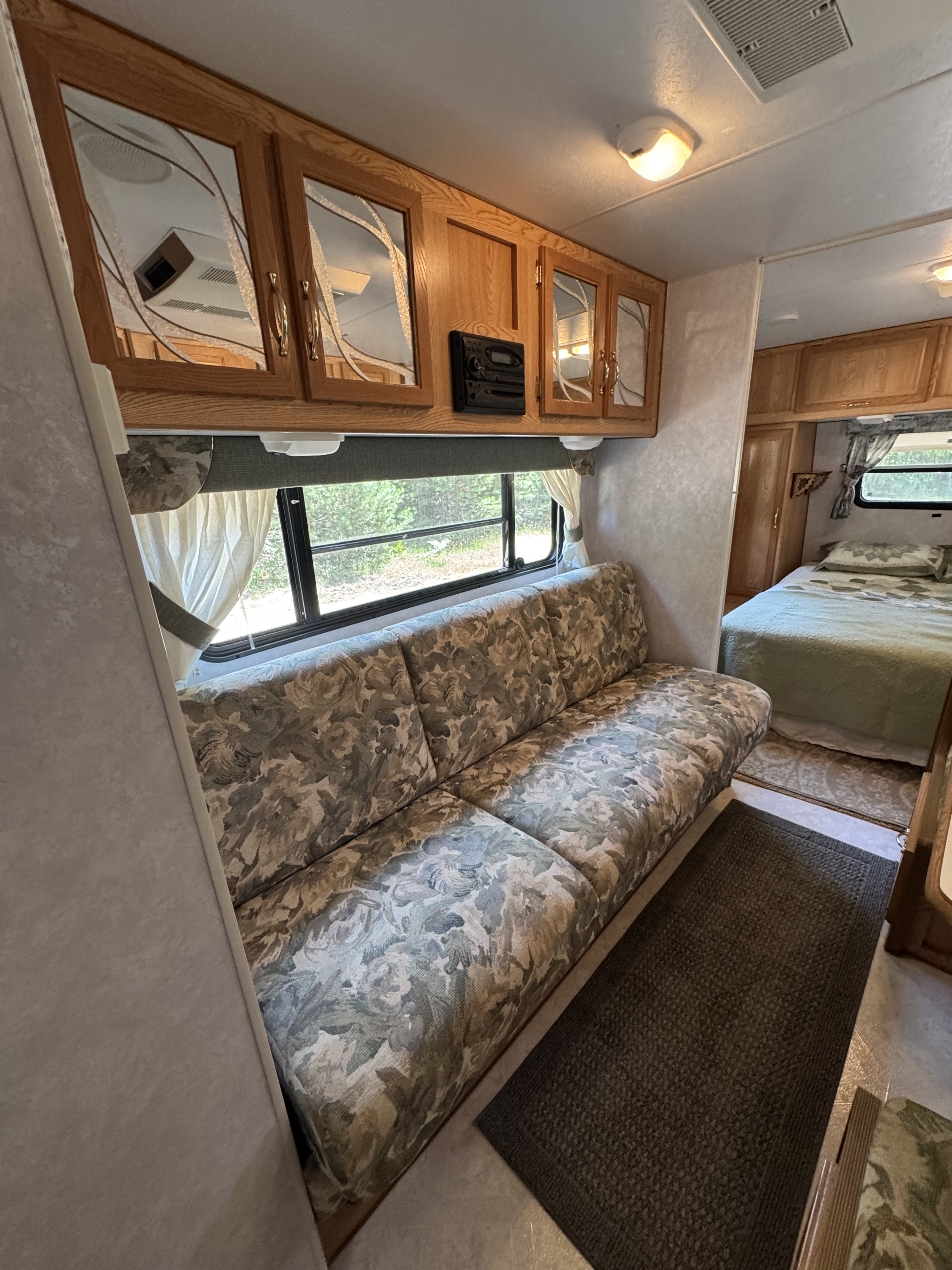Cozy rv rental interior featuring a floral couch, wood cabinets, windows, and a glimpse of the bedroom. Ready for your next adventure.. Sunline Solaris Lite 2000