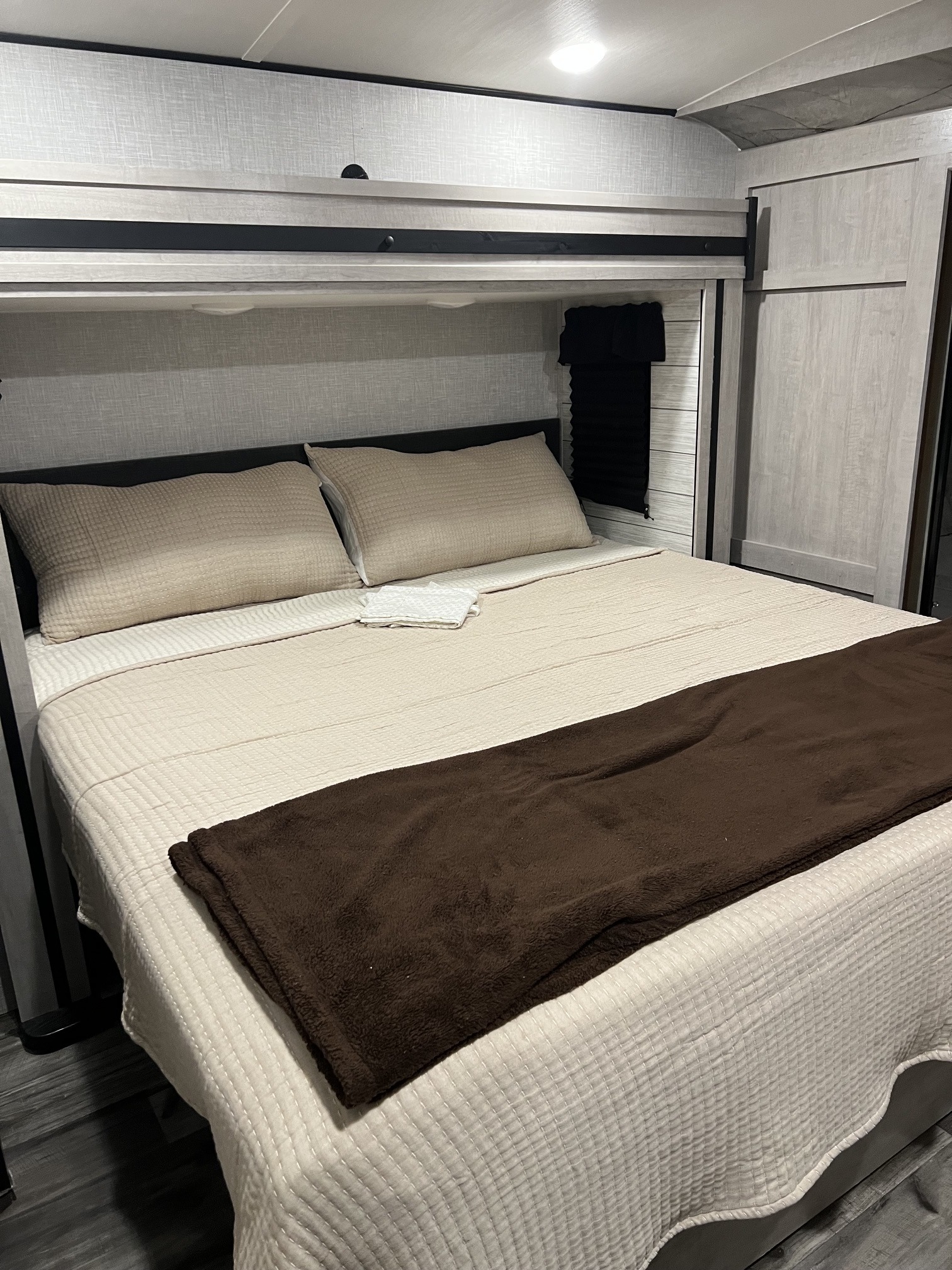 Cozy RV rental bedroom with a comfortable bed, cream quilted bedding, beige pillows, and a brown blanket.. Crossroads RV Sunset Trail 2023