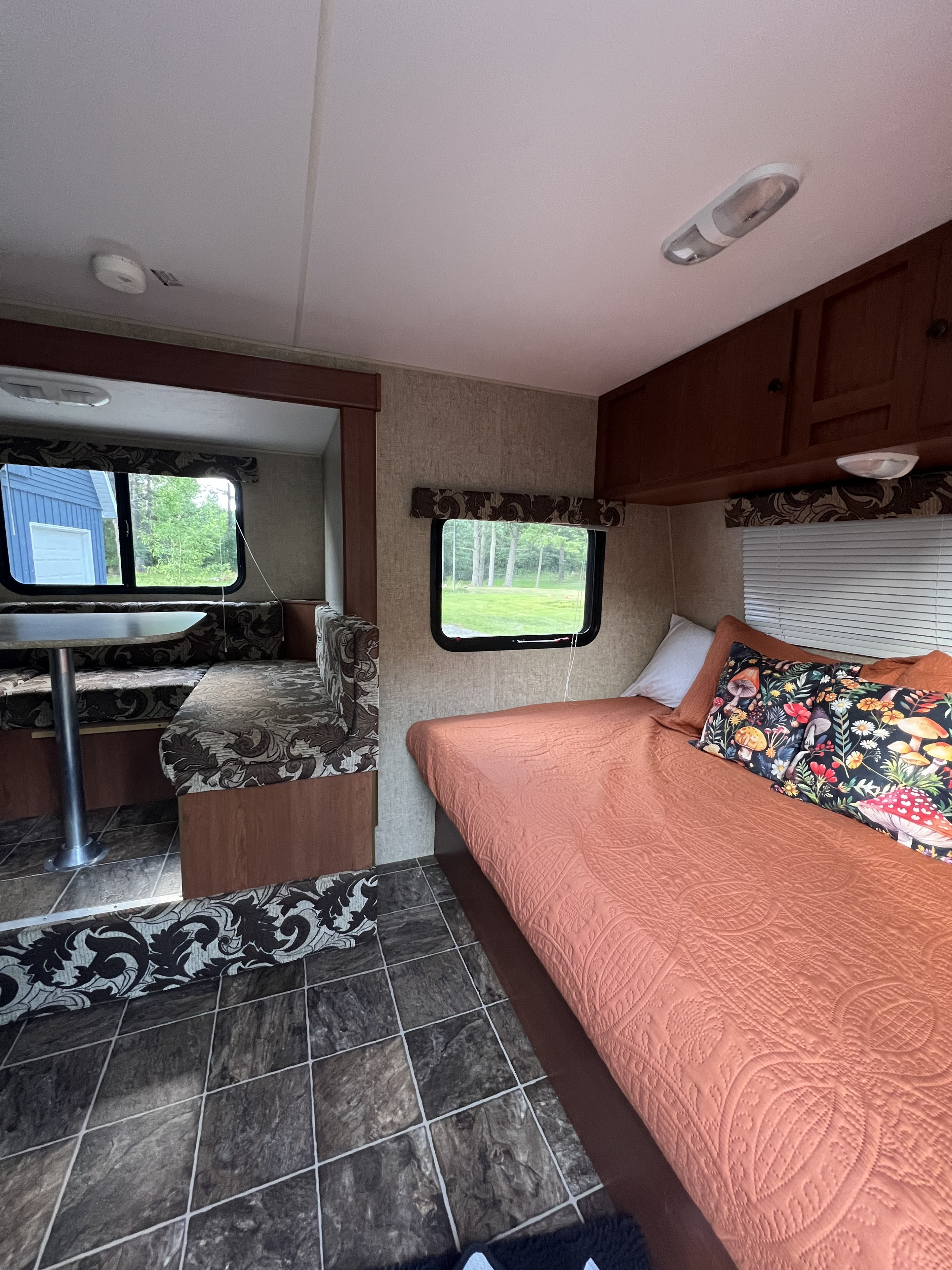 Cozy RV rental interior with a patterned dining booth and bed, featuring windows, tiled floor, and ceiling fixtures.. Sportsmen Classic 2014