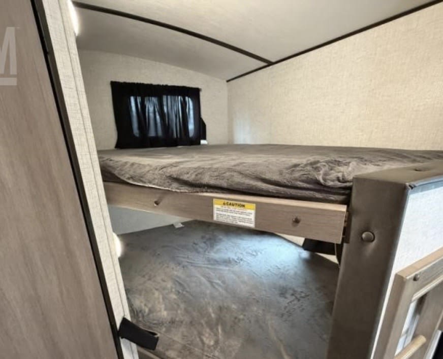 Compact RV rental sleeping area featuring bunk beds with grey bedding and a window. Ideal for a family camper.. Crossroads RV Sunset Trail Super Lite 2022