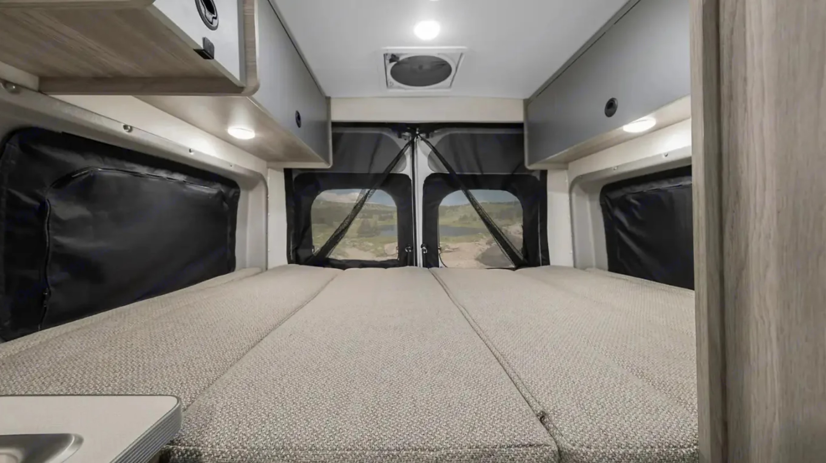 An RV rental's rear interior with a fold-out bed, open doors to nature, and overhead storage.. Winnebago Solis 2023