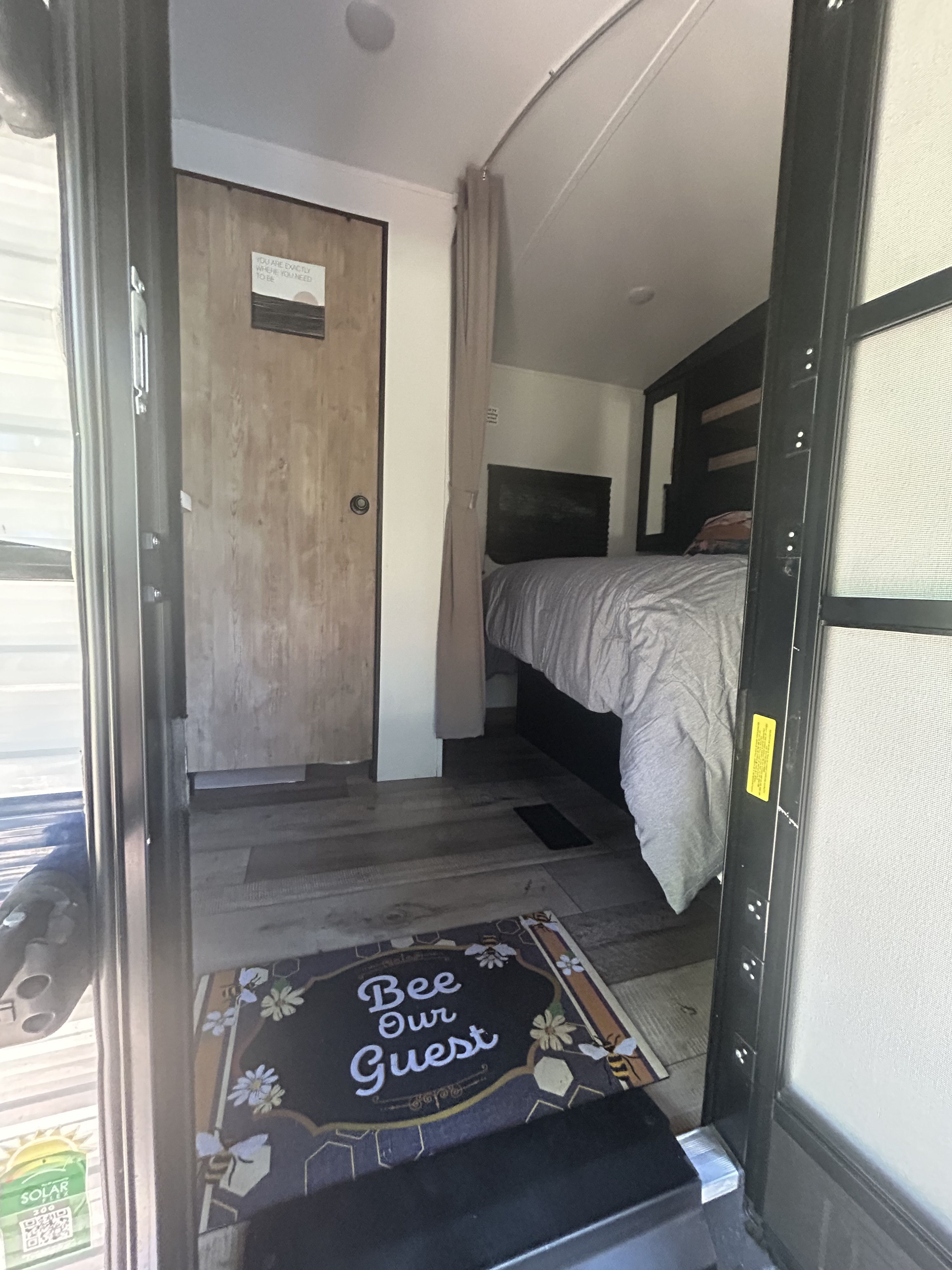 Inviting RV rental interior: "Bee Our Guest" mat, encouraging door sign, privacy curtain, and cozy bedroom awaits.. Keystone RV Springdale 2022