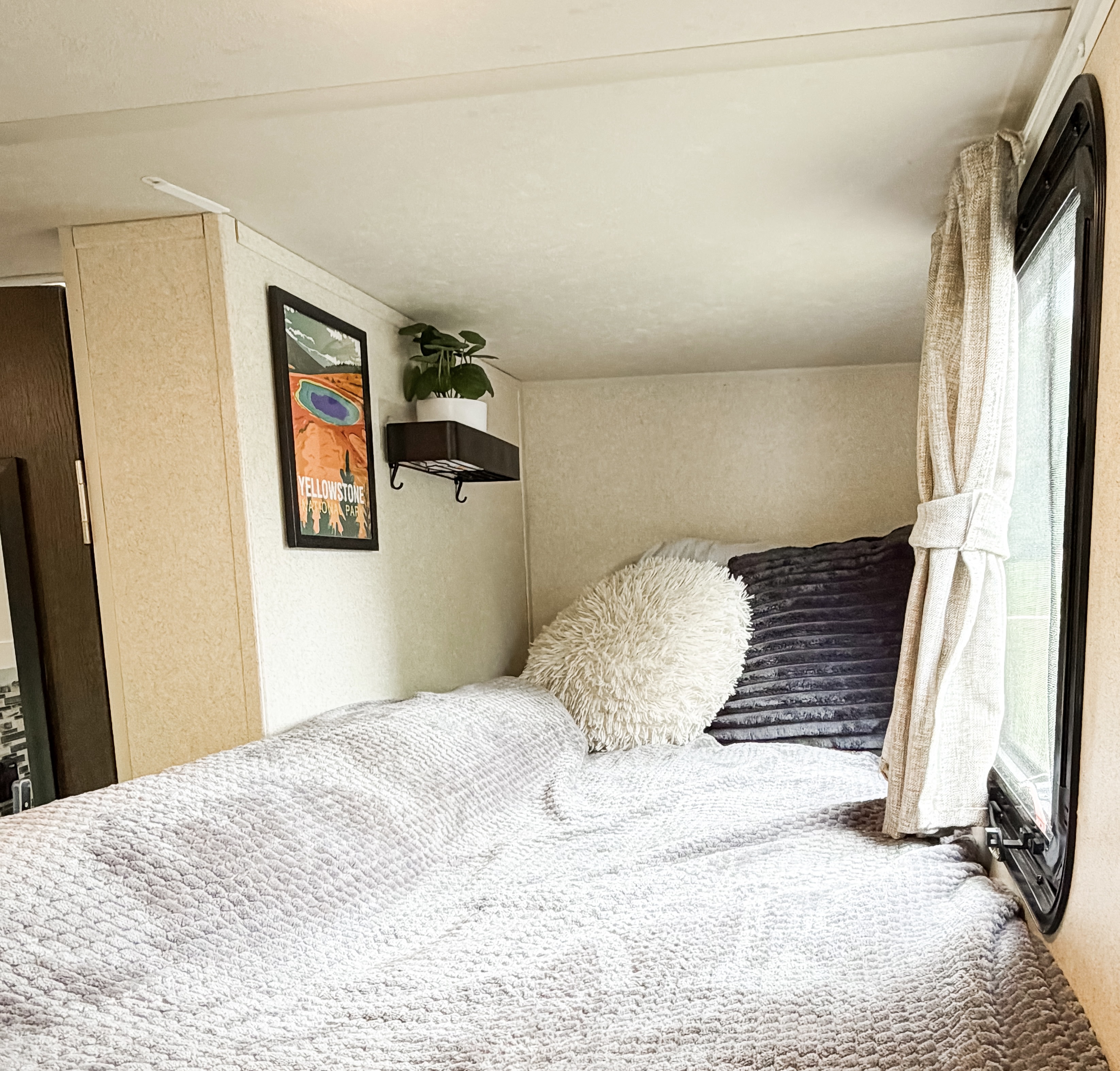 Cozy RV rental bed with soft textures, a window, plant shelf, and Yellowstone poster, perfect for comfortable travel.. Forest River Salem FSX 2018