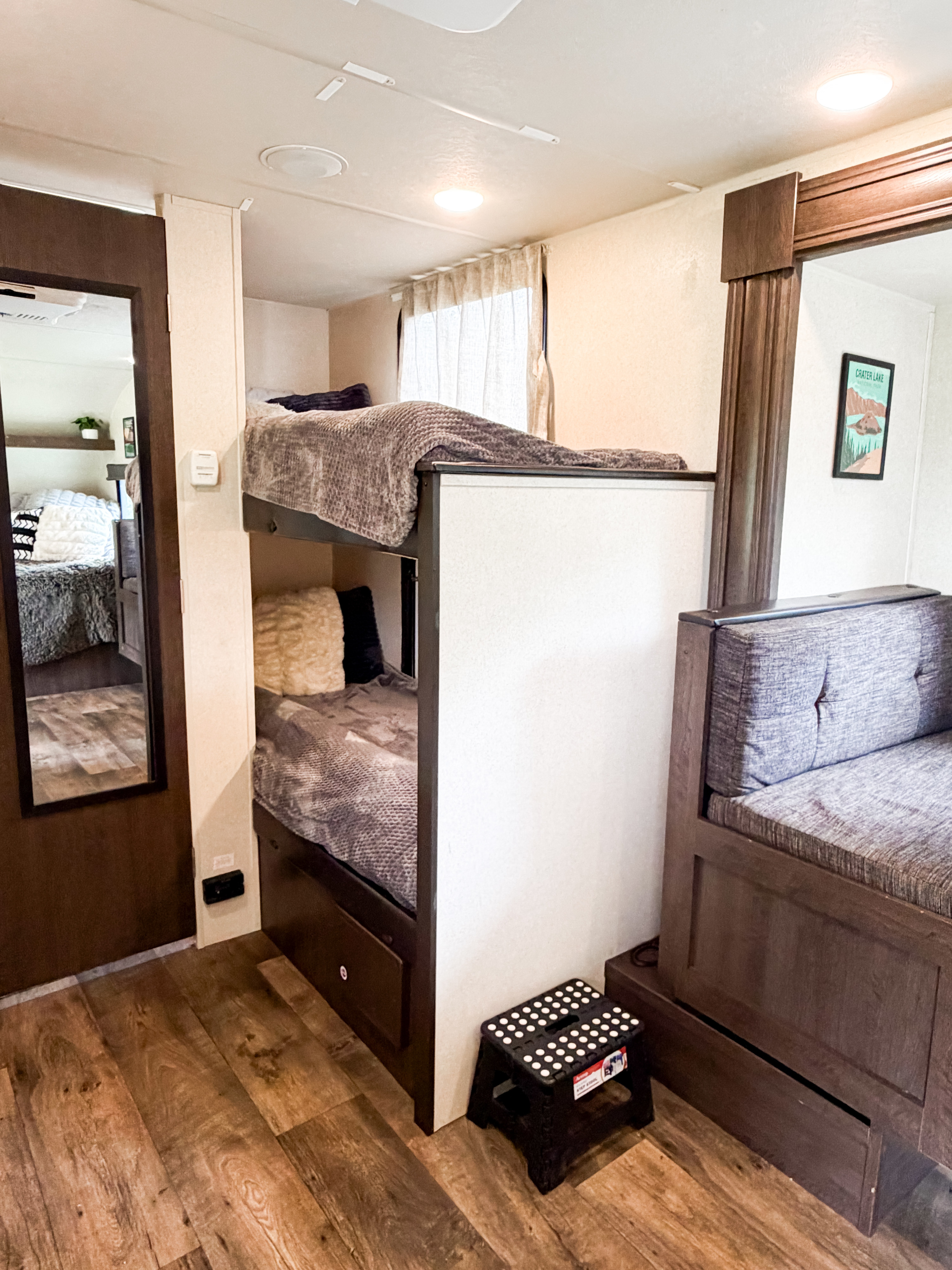 Inside a bright RV rental: twin bunk beds with blankets, a small seating area, and wood floors. Ideal for compact living and travel.. Forest River Salem FSX 2018