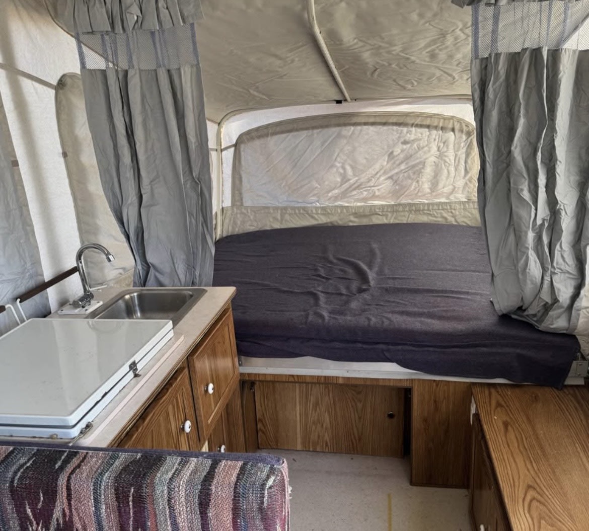 RV rental interior: A pop-up camper's cozy sleeping area, sink, covered stove, and storage cabinets.. Coleman Destiny Rio Grande 1995