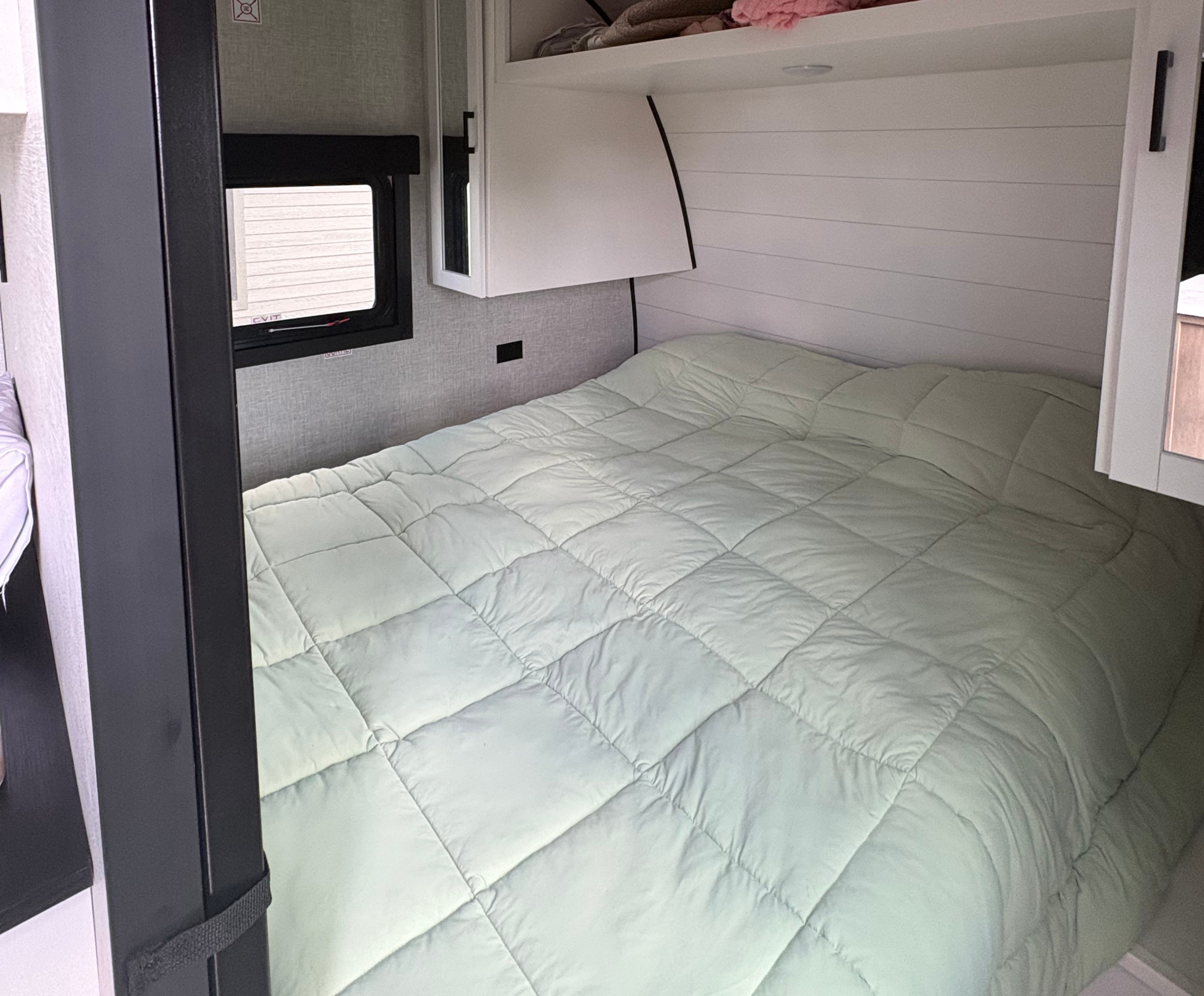 Cozy RV rental bedroom with a light green comforter, white headboard, window, and overhead storage. Ready for your trip.. FR3 FR3 Motorhome 2021