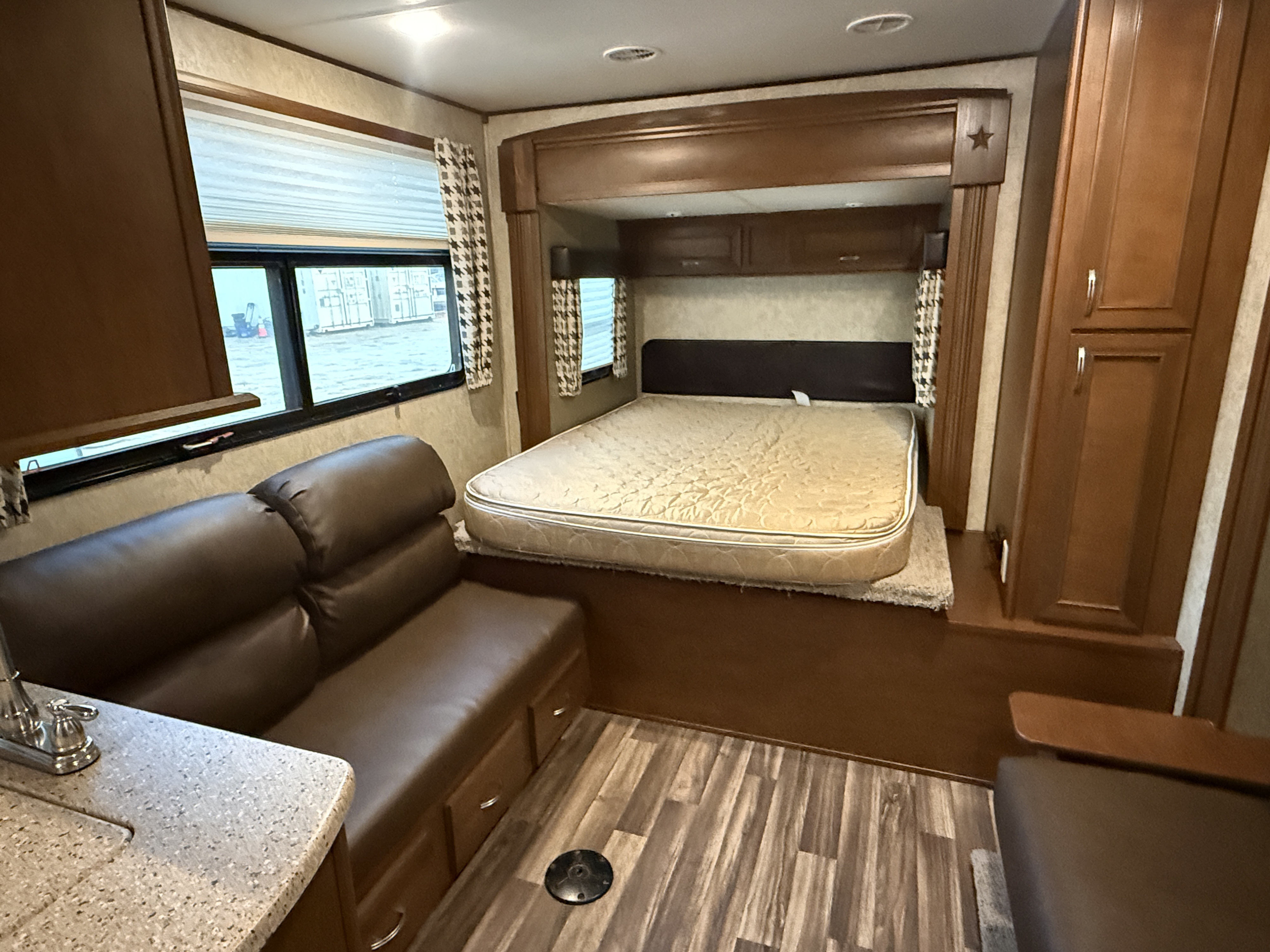 RV rental interior with a raised bed, dark sofa, and light counter with sink. Wood accents and laminate floor.. Highland Ridge Highlander 2016