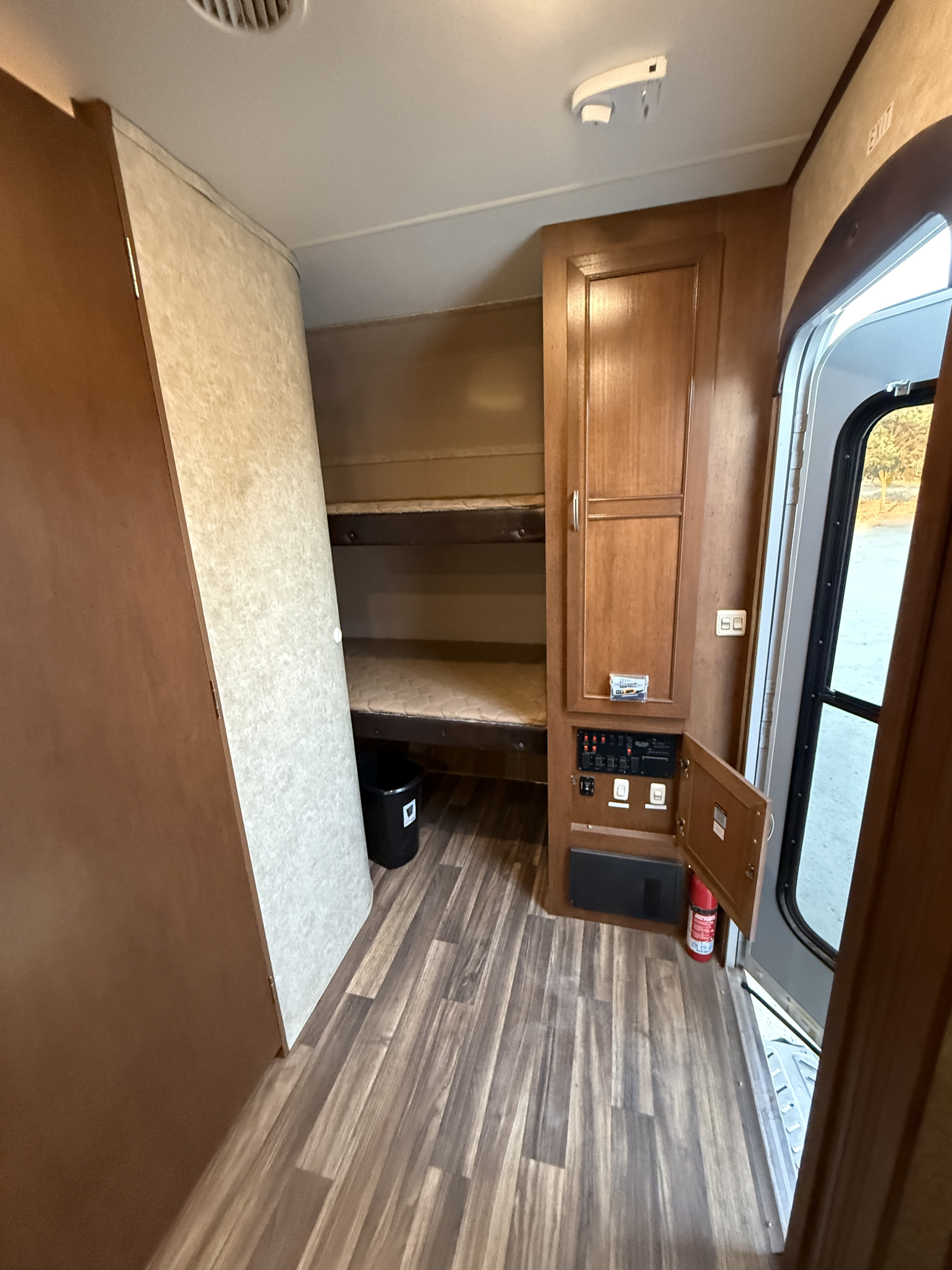 This RV rental interior features dual bunk beds, an electrical control panel, and a fire extinguisher by the open exit door.. Highland Ridge Highlander 2016