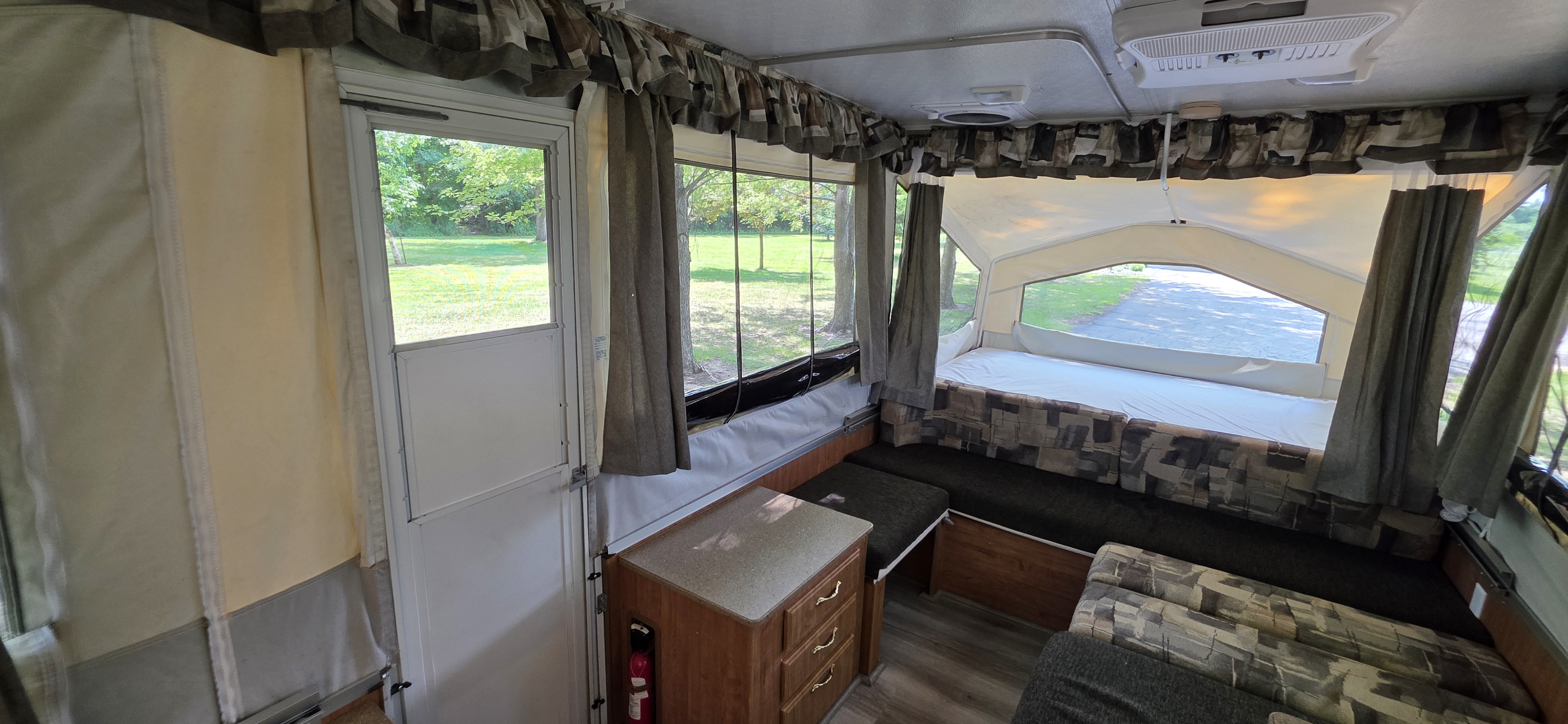 Inside an RV rental: a pop-up camper's interior with a bed, patterned dinette, and cabinet, offering a serene view of trees outside.. Forest River Rockwood Freedom 2008