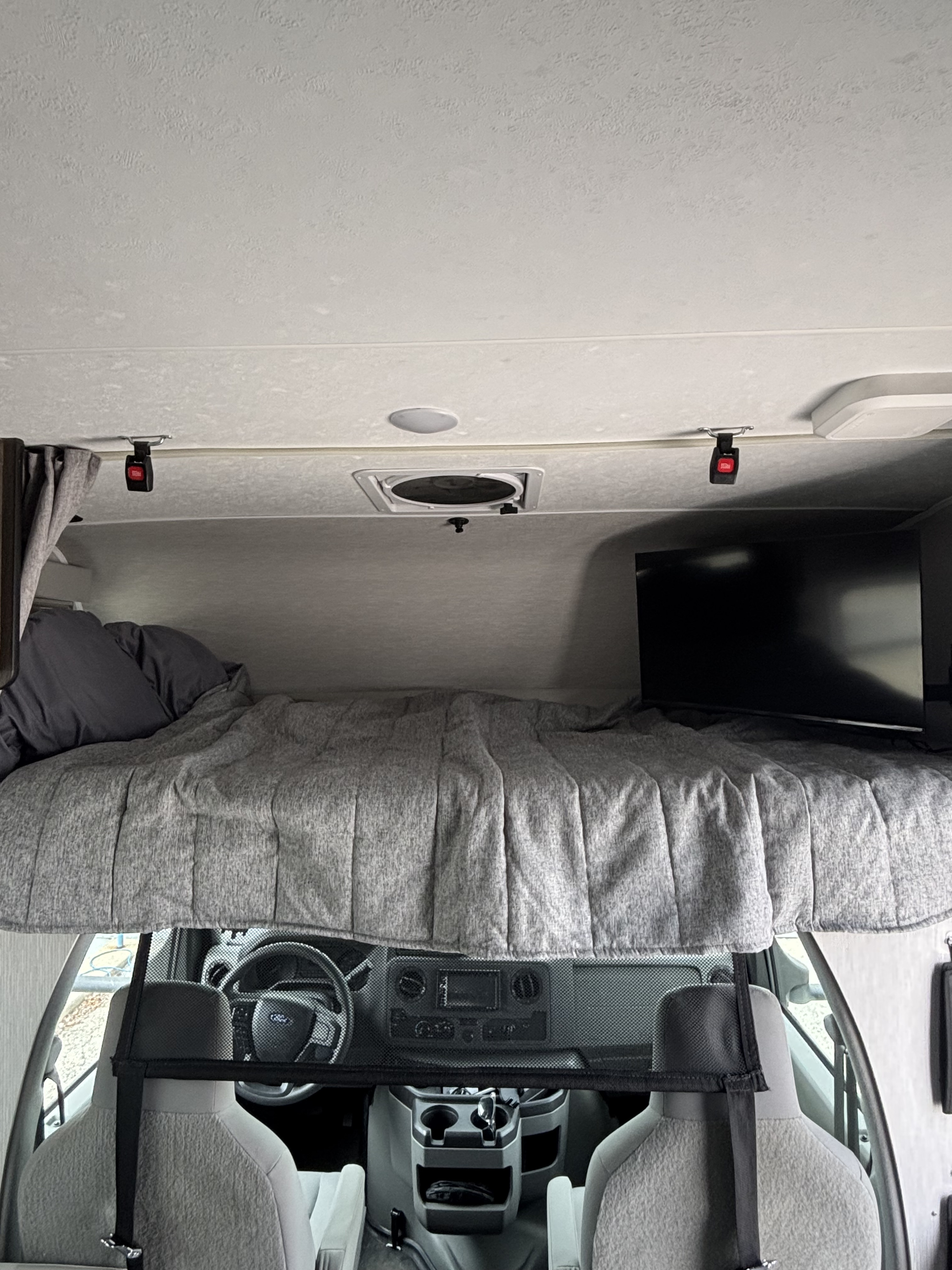 RV rental interior: A cozy over-cab bunk bed with gray bedding and a TV, overlooking the Ford driver's cabin.. Coachman Cross Trail 22xg 2023