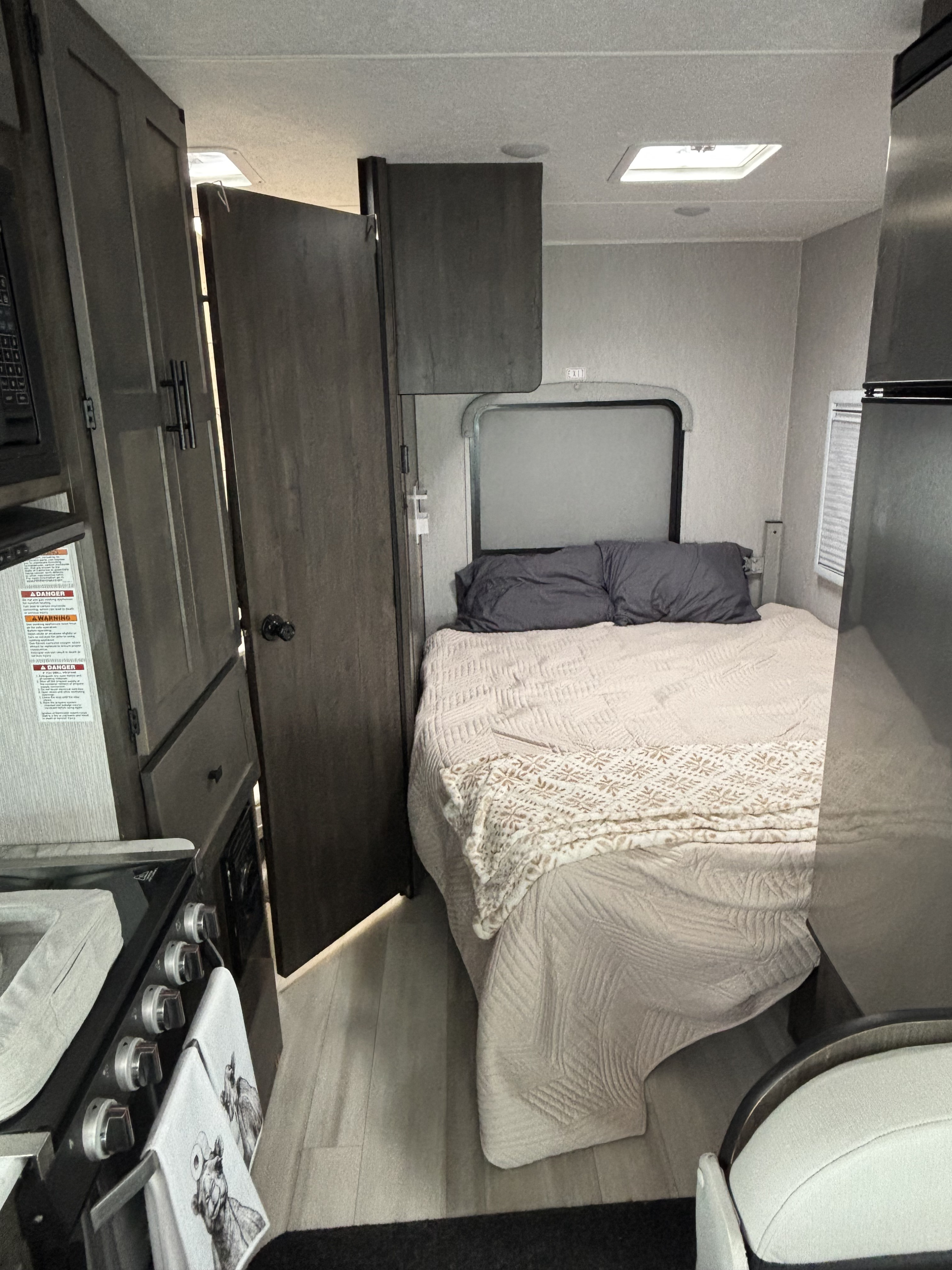 Inside a compact RV rental, showing the bedroom area with a bed and a partial view of the kitchenette.. Coachman Cross Trail 22xg 2023
