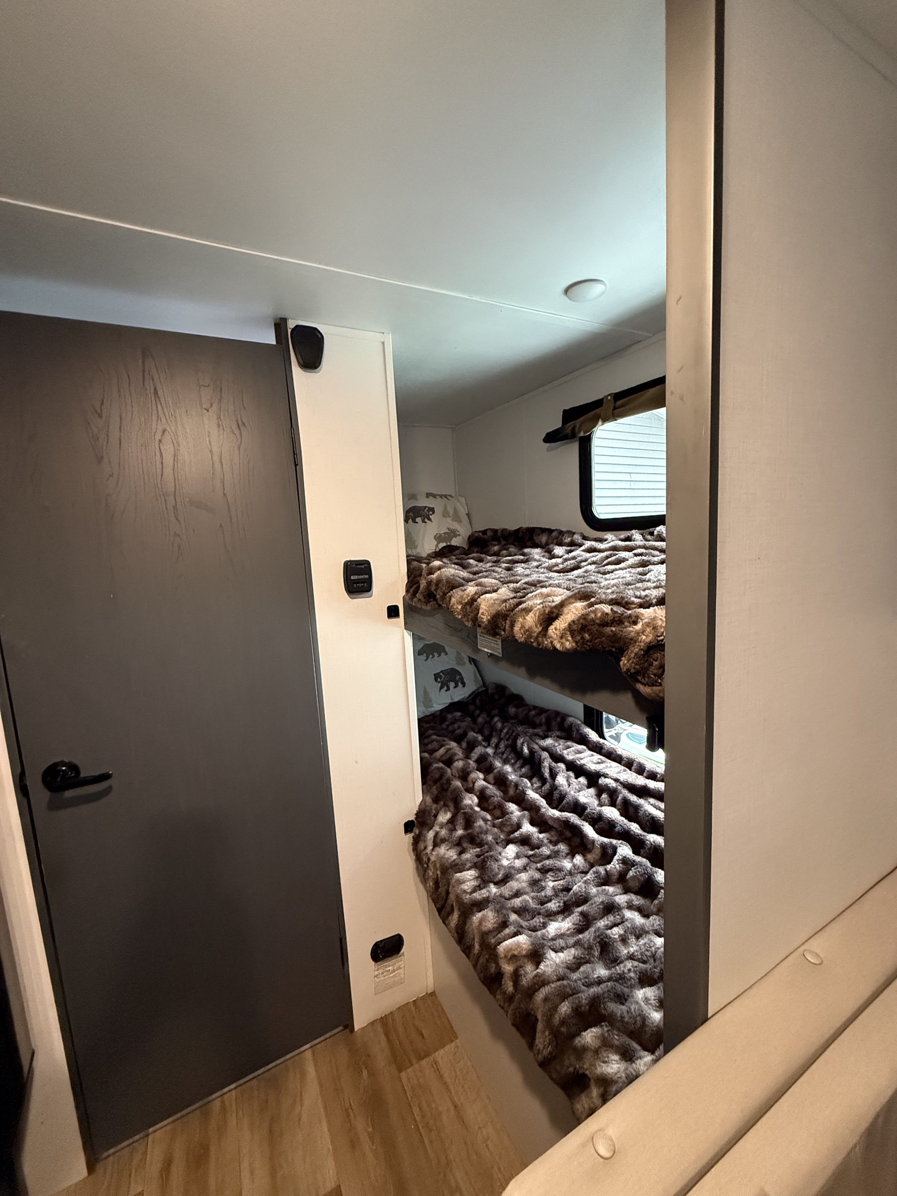Inside an rv rental: cozy bunk beds with plush blankets and a window. A dark door on the left completes this comfortable space.. Keystone RV Bullet Crossfire 2024
