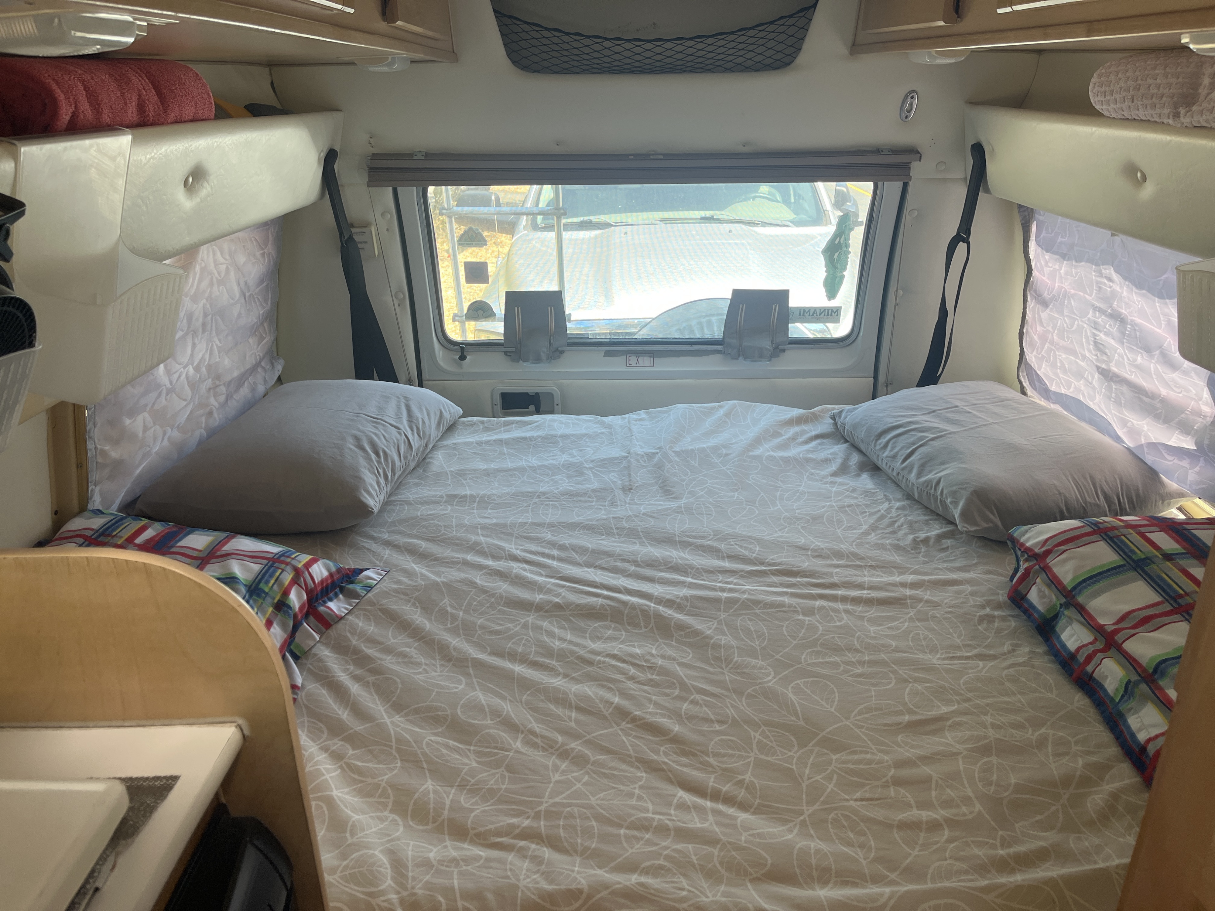Cozy RV rental bedroom with patterned duvet, pillows, and a view through the back window, perfect for resting.. Dodge Leisure Travel Wide Body 2002