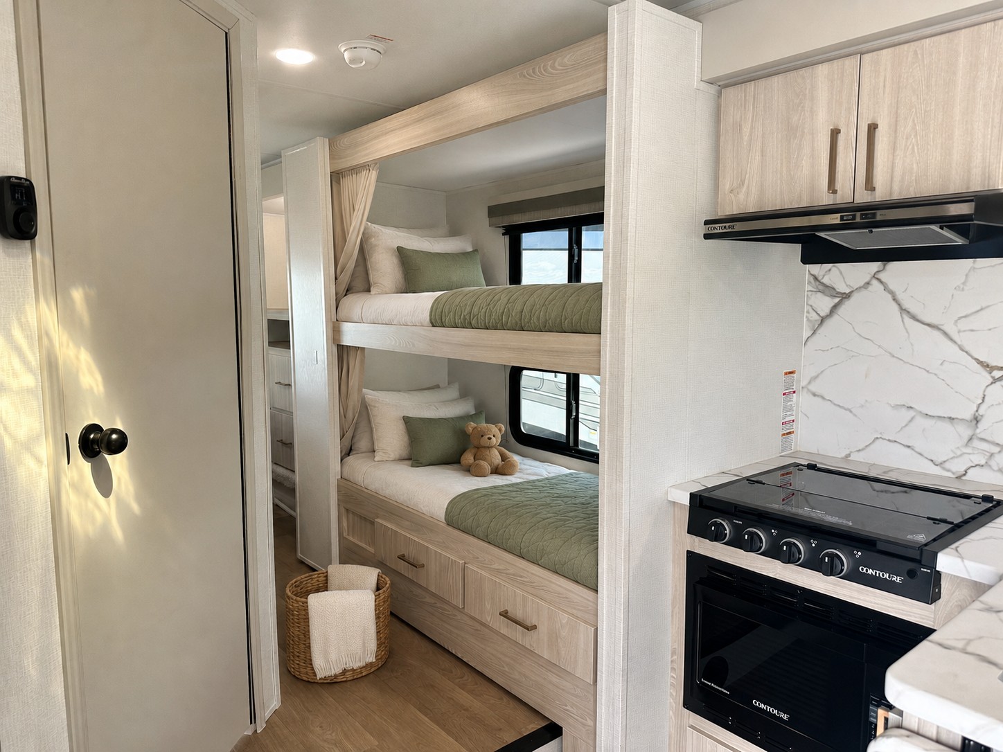 Modern RV rental bunk beds with sage green bedding and a compact kitchen area featuring a stove and oven. Ideal family space.. East to West Entrada 2026
