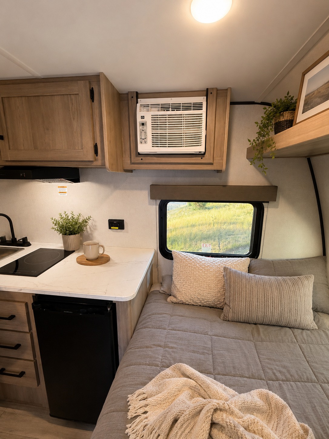 Inside a modern RV rental: compact kitchen with cooktop, mini-fridge, built-in AC, and a cozy bed by a window with blankets.. Keystone RV Coleman 2026