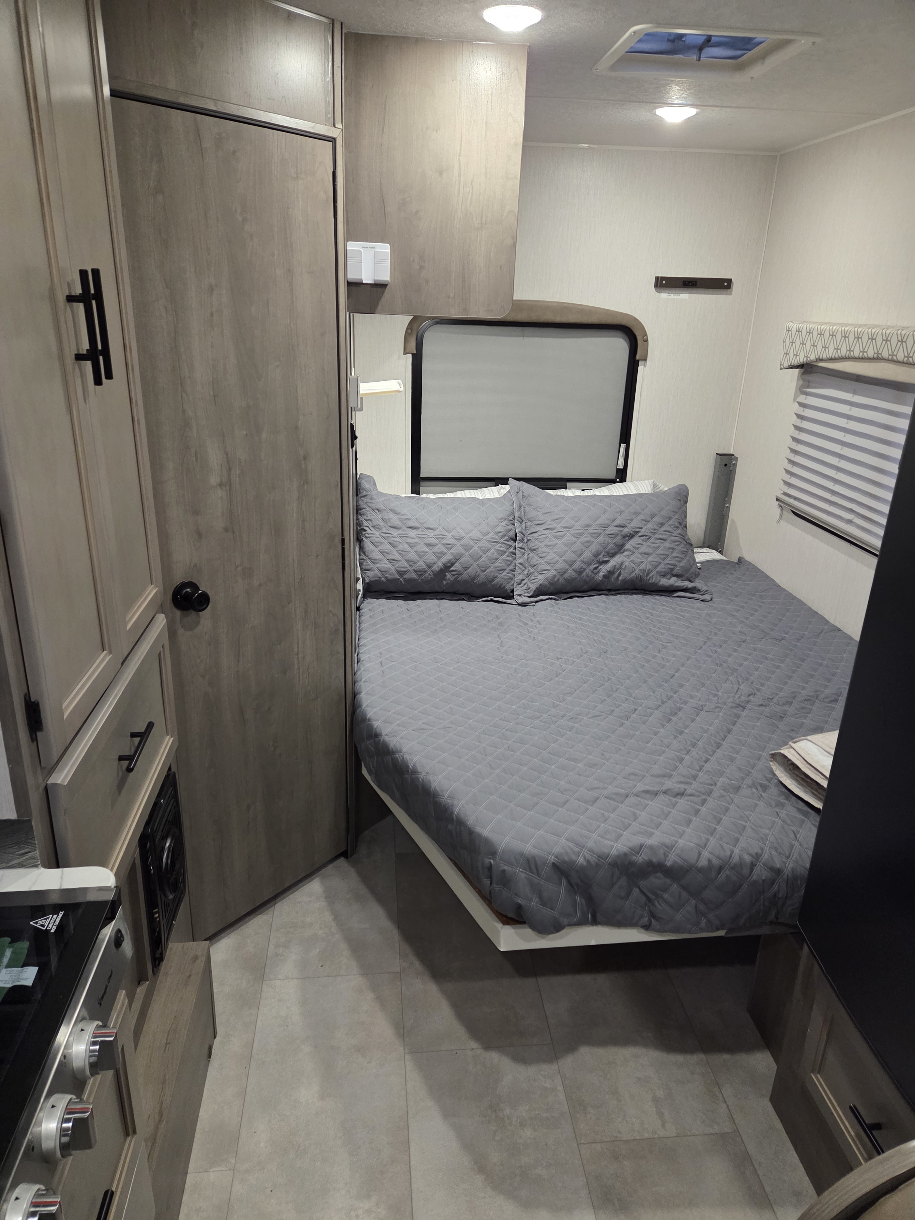 This RV rental offers a cozy bedroom area with a gray quilted bed, wood cabinets, and a visible stovetop for travel comfort.. Forest River Coachmen Freelander 2020
