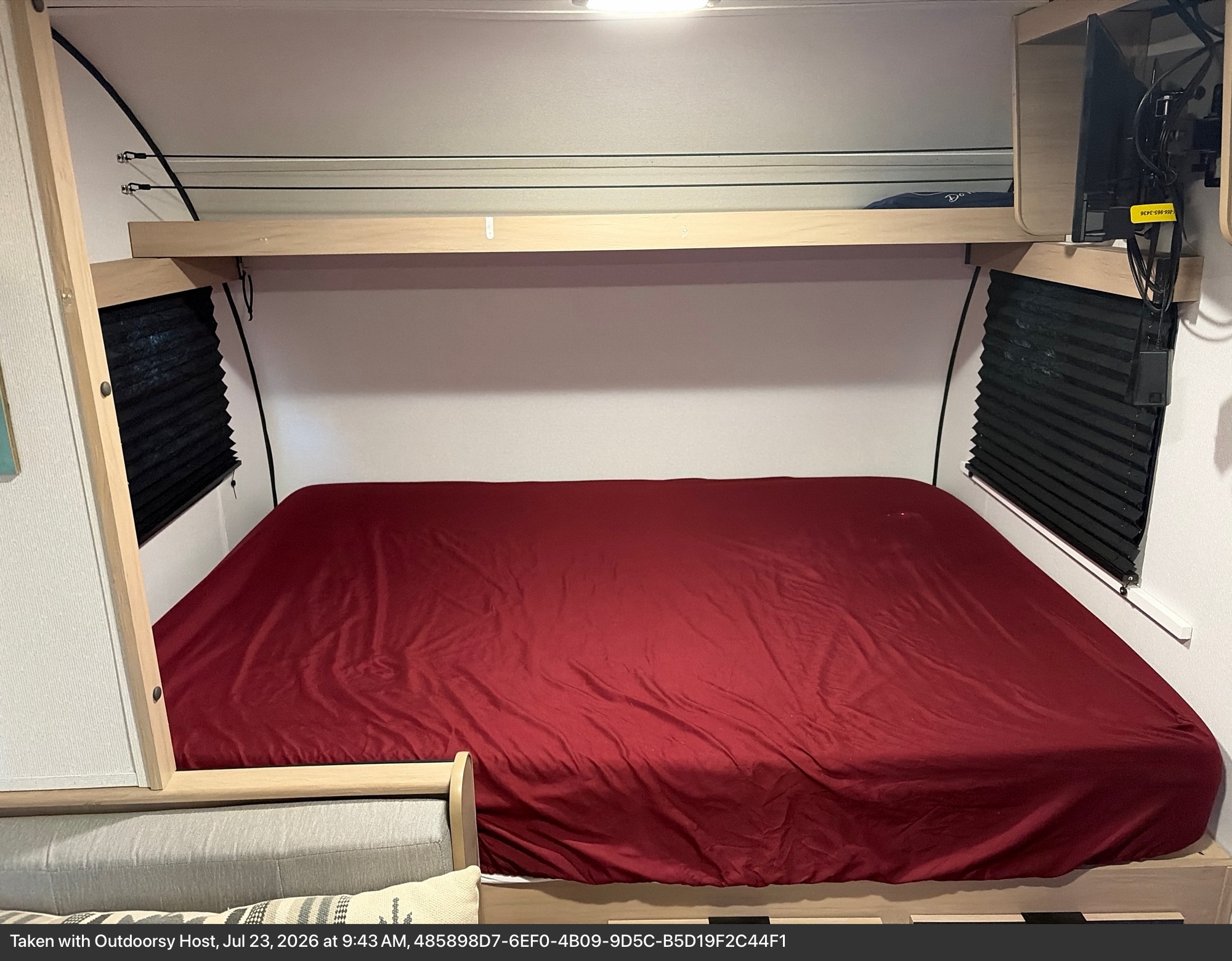 RV rental bedroom: cozy bed with red sheets, overhead shelf, mounted TV, and side window blinds for comfort.. Cruiser RV Hitch 17 BHS 2021